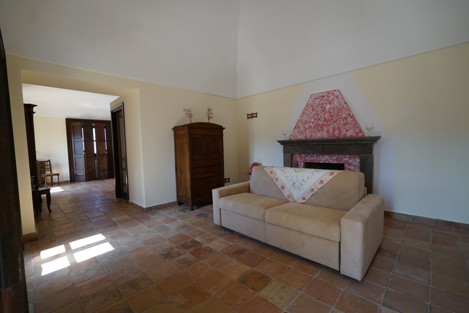 Cozy living room featuring a beige sofa, a traditional fireplace with pink tiles, and rustic wooden furniture. The space has natural light flowing through large windows, enhancing the warm ambiance. | Only on SopranoVillas