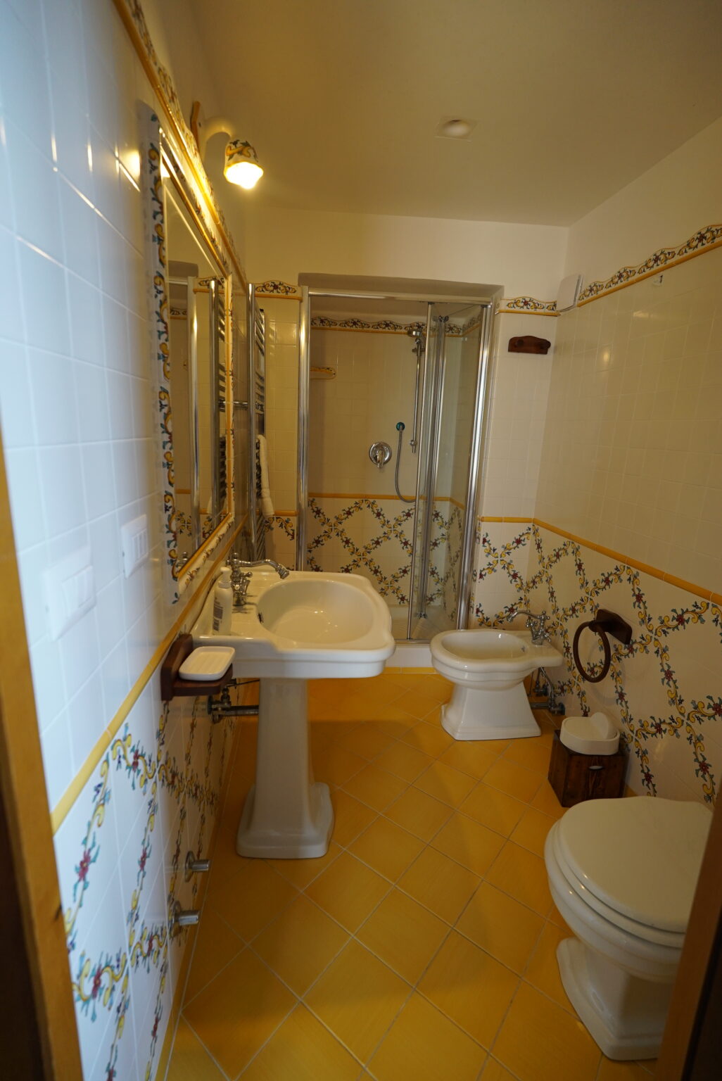Modern bathroom featuring a shower, sink, and toilet, with decorative tile accents and a bright yellow floor. | Only on SopranoVillas