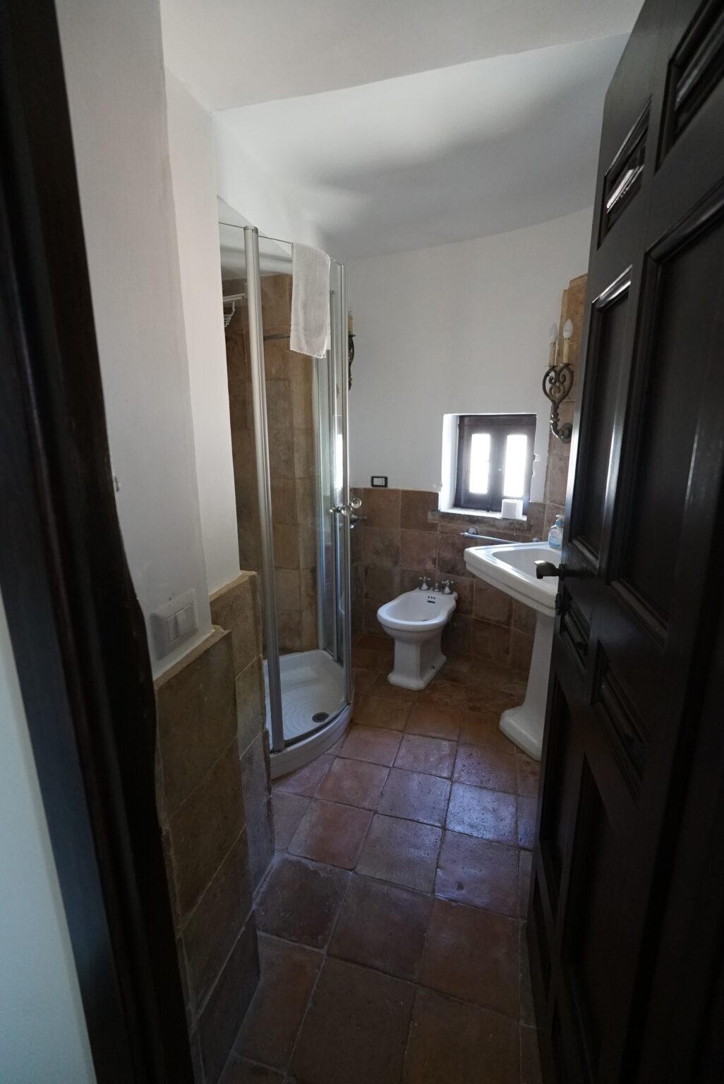 Modern bathroom featuring a shower, sink, and toilet, with tiled flooring and natural light from a window. | Only on SopranoVillas