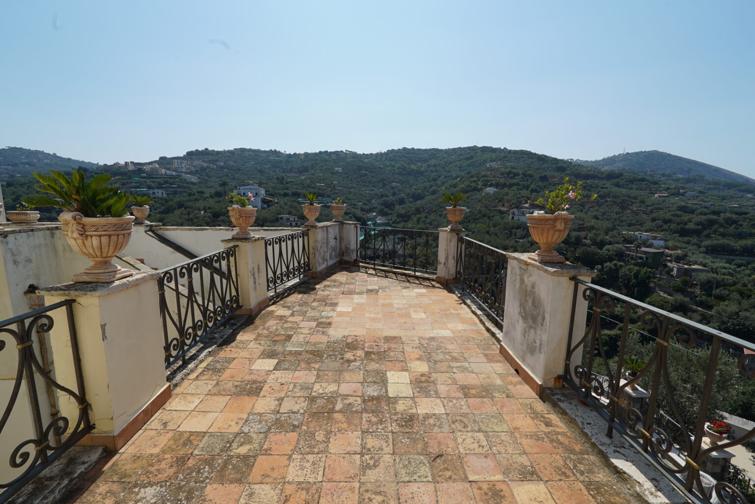 Scenic terrace view overlooking lush hills with decorative planters and a clear blue sky, ideal for outdoor relaxation. | Only on SopranoVillas