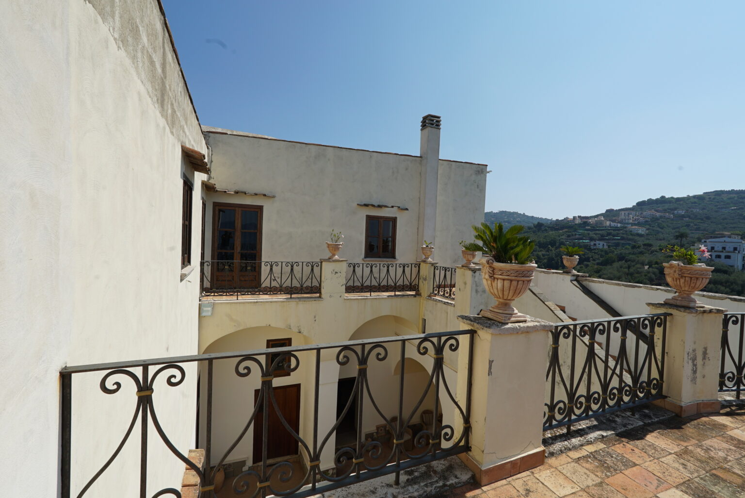 Historic building with a balcony overlooking a hillside, featuring decorative planters and a clear blue sky. Ideal for showcasing architectural design and scenic views. | Only on SopranoVillas