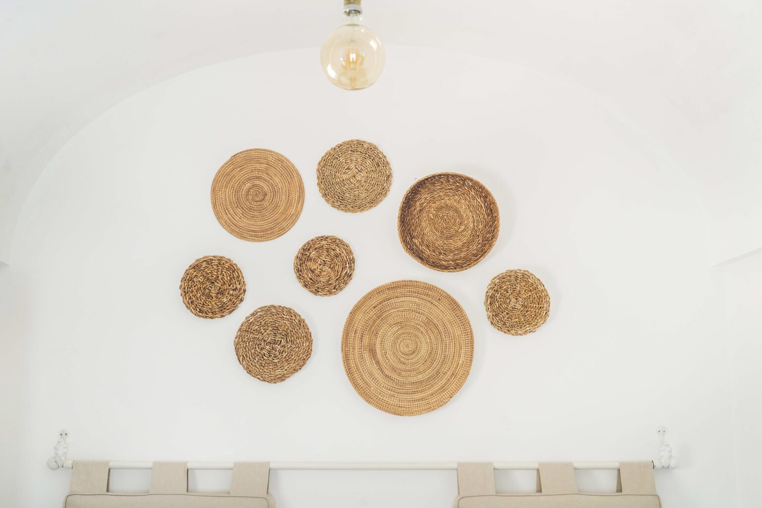 Woven wall decor featuring a variety of round, natural fiber baskets arranged artistically on a white wall, creating a minimalist and stylish interior design element. | Only on SopranoVillas