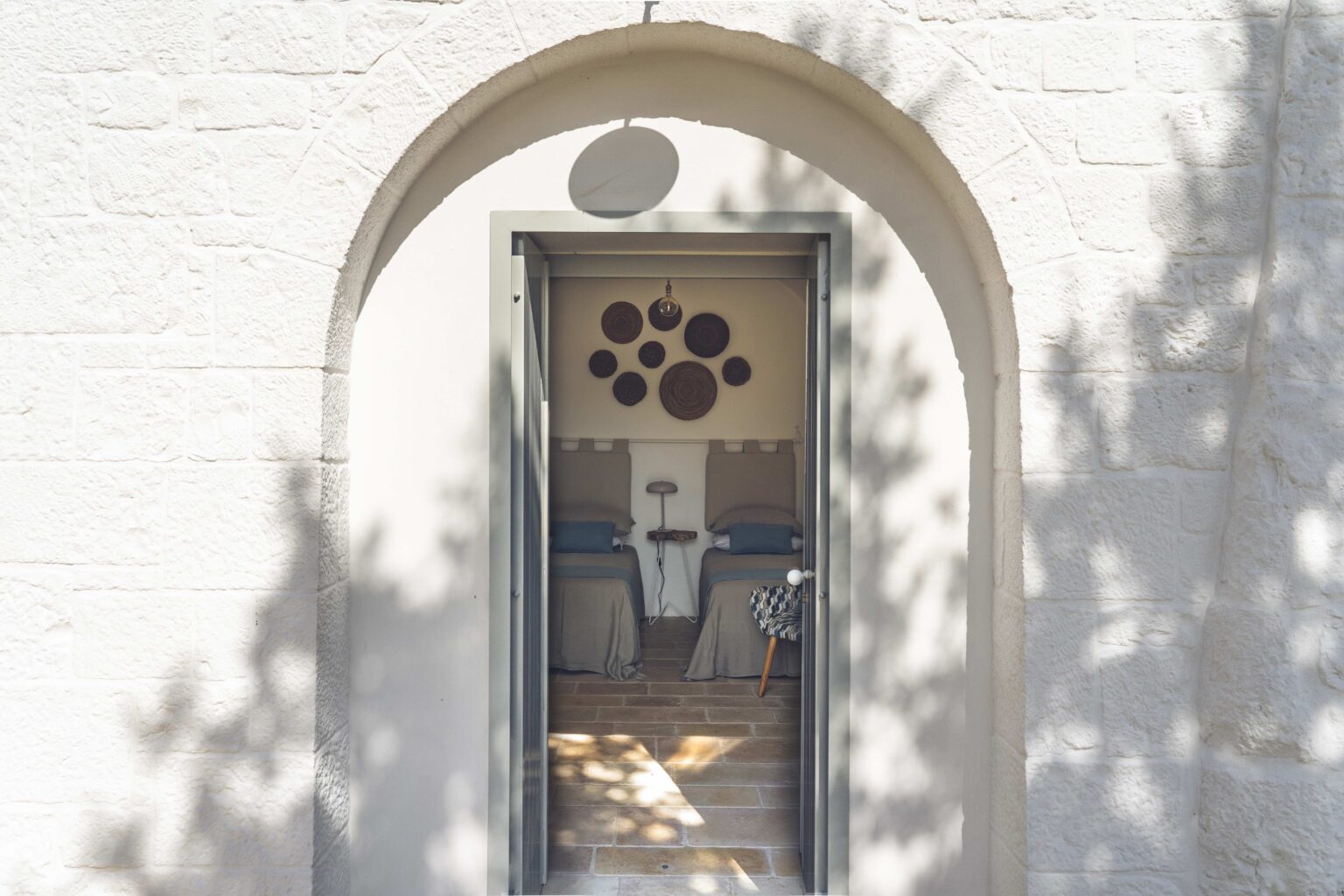 Modern entrance door framed by a decorative arch, showcasing unique wall art and wooden flooring visible through the doorway. Natural light casts shadows on the textured exterior wall. | Only on SopranoVillas