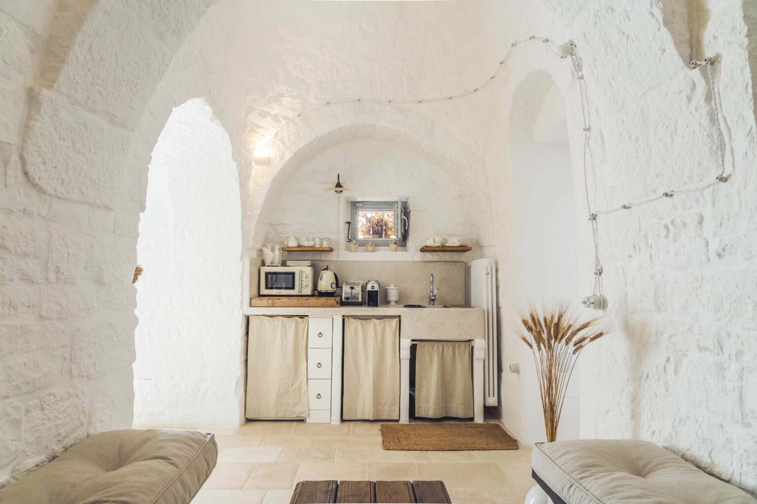 Cozy kitchen area with arched stone walls, featuring a microwave, coffee maker, and a sink. The space includes wooden shelves with dishware and natural decor, creating a warm and inviting atmosphere. | Only on SopranoVillas