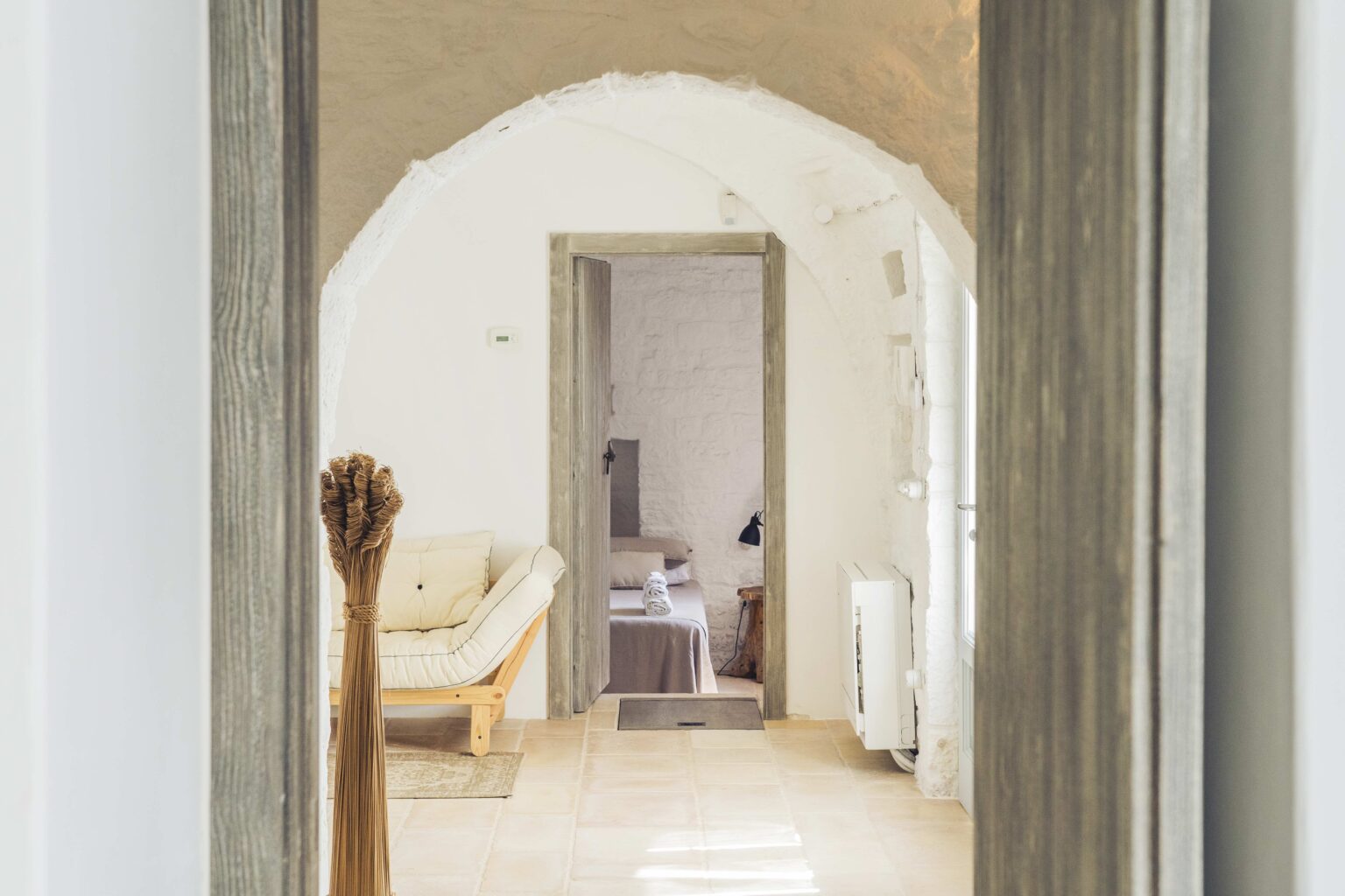 Interior view of a cozy, modern living space with a neutral color palette, featuring an arched doorway leading to a bedroom. Natural light enhances the warm atmosphere, complemented by minimalist decor and a comfortable seating area. | Only on SopranoVillas