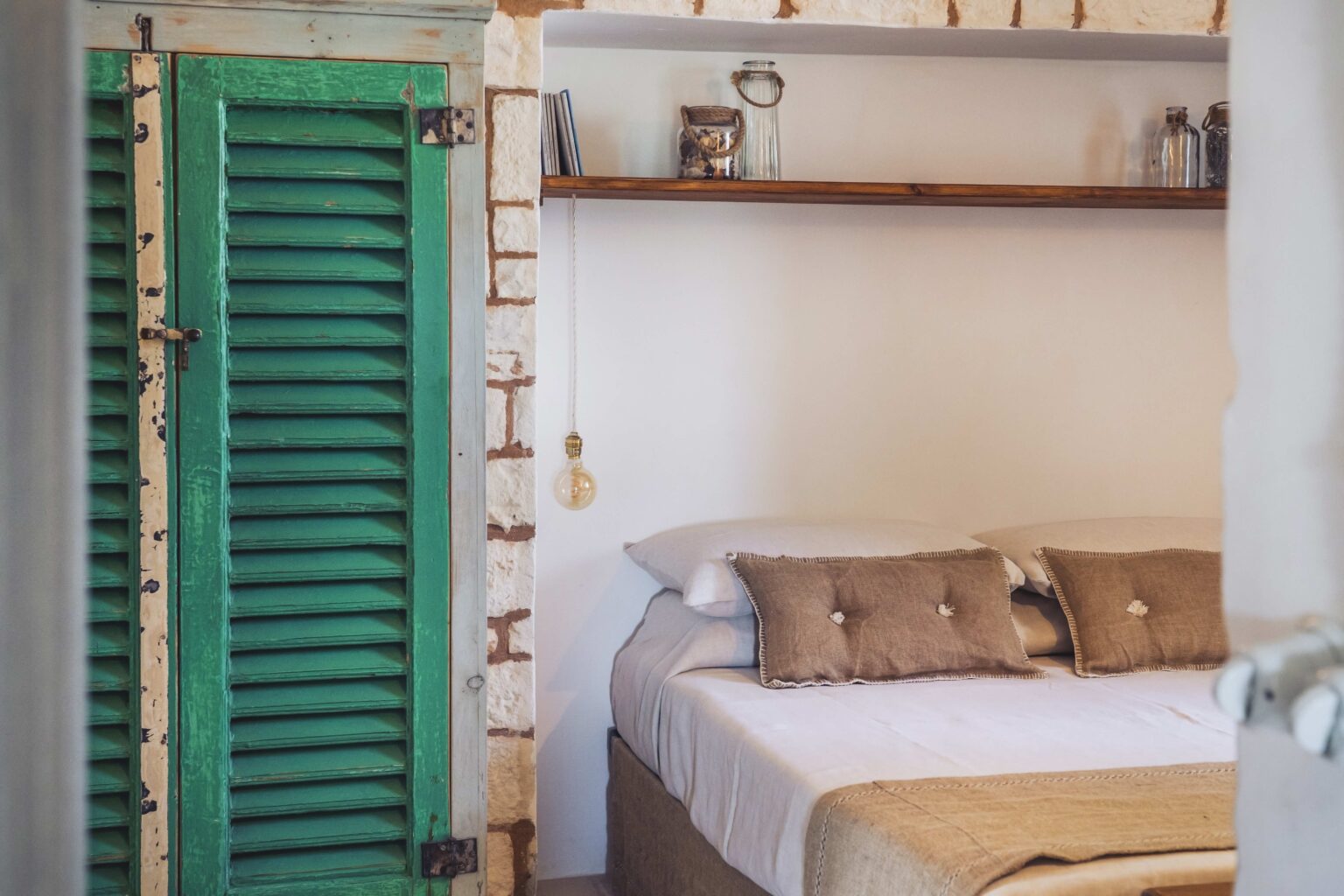Cozy bedroom interior featuring a comfortable bed with decorative pillows, a rustic wooden shelf, and a vibrant green shutter door. The room has a warm, inviting atmosphere with soft lighting. | Only on SopranoVillas