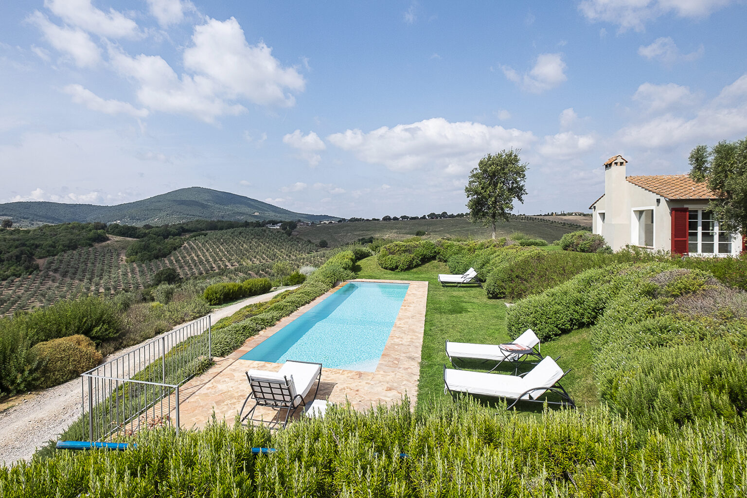 Scenic view of a luxurious villa with a swimming pool, surrounded by lush greenery and rolling hills under a blue sky, ideal for a relaxing getaway. | Only on SopranoVillas