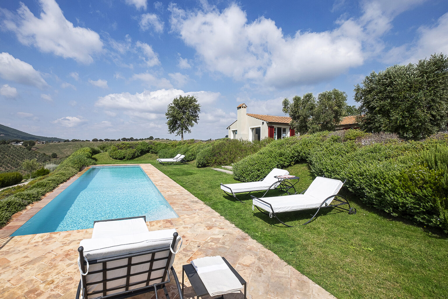 Scenic view of a serene villa with a swimming pool surrounded by lush greenery and blue skies, ideal for relaxation and outdoor living. | Only on SopranoVillas