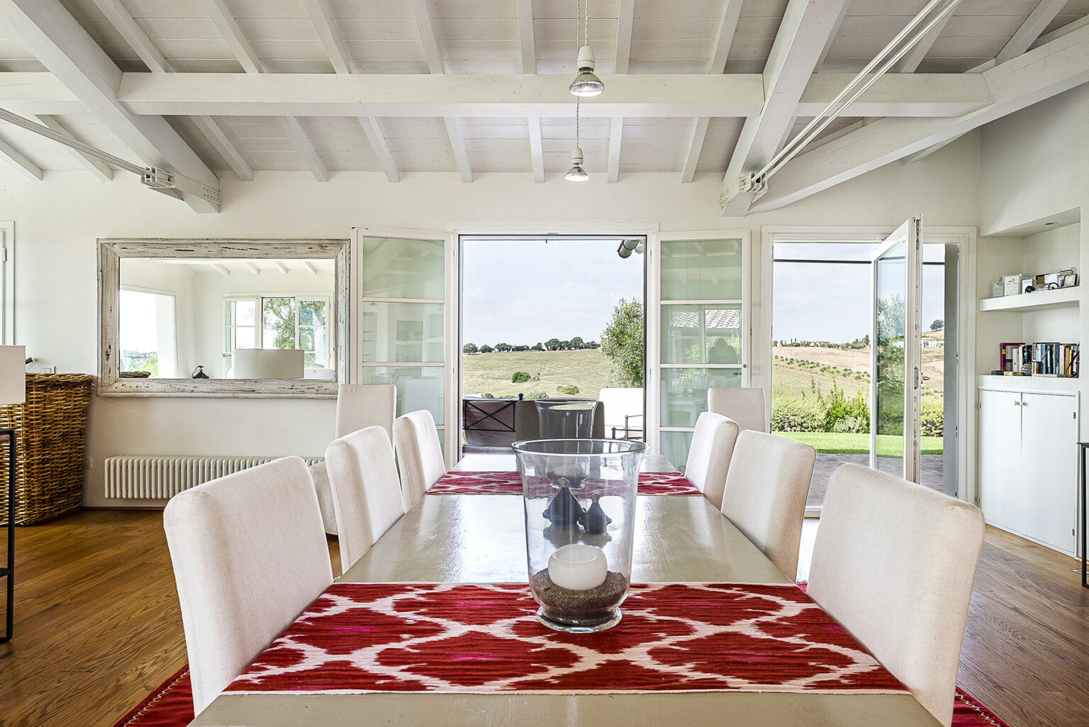 Bright and airy dining room featuring a large table with white chairs, a red patterned rug, and large open doors leading to a scenic outdoor view. | Only on SopranoVillas