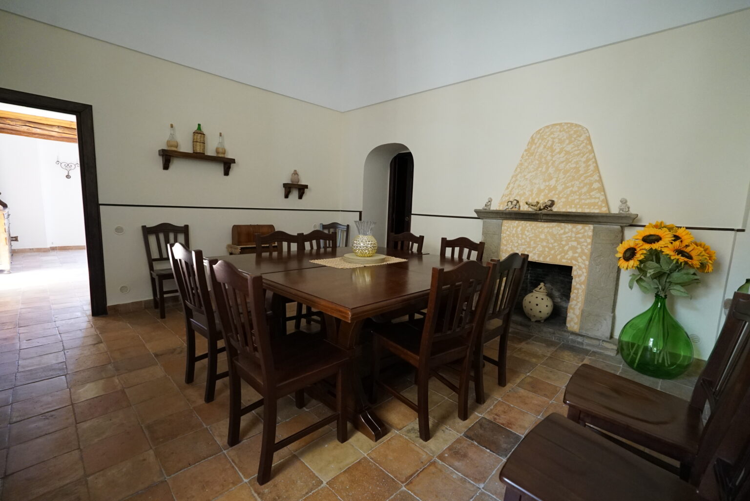 Spacious dining room featuring a large wooden table surrounded by chairs, with a stone fireplace and decorative elements, complemented by a vase of sunflowers. | Only on SopranoVillas