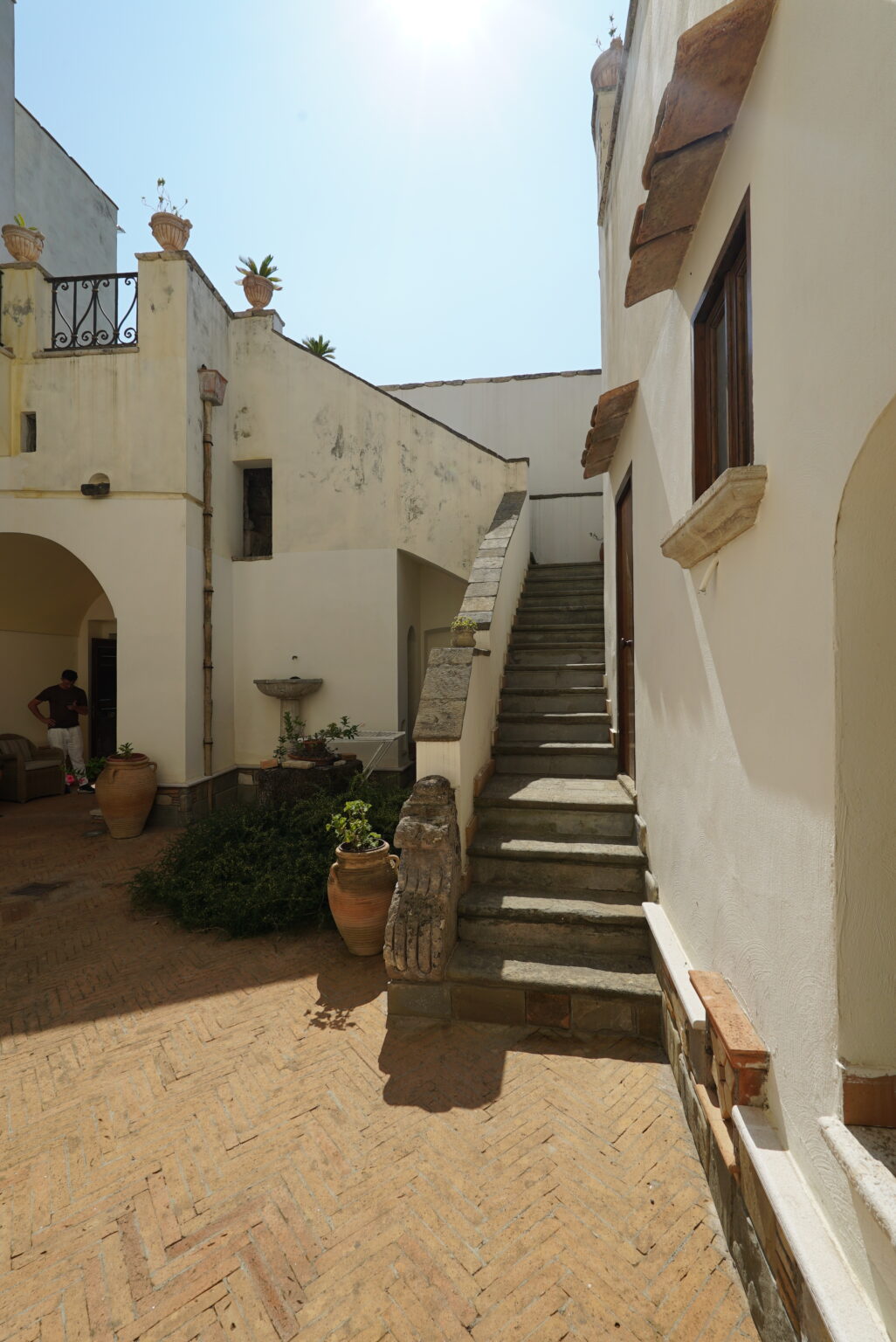 Stone staircase leading to an upper level in a rustic courtyard, surrounded by whitewashed walls and potted plants. A fountain can be seen in the background, adding to the serene atmosphere. | Only on SopranoVillas