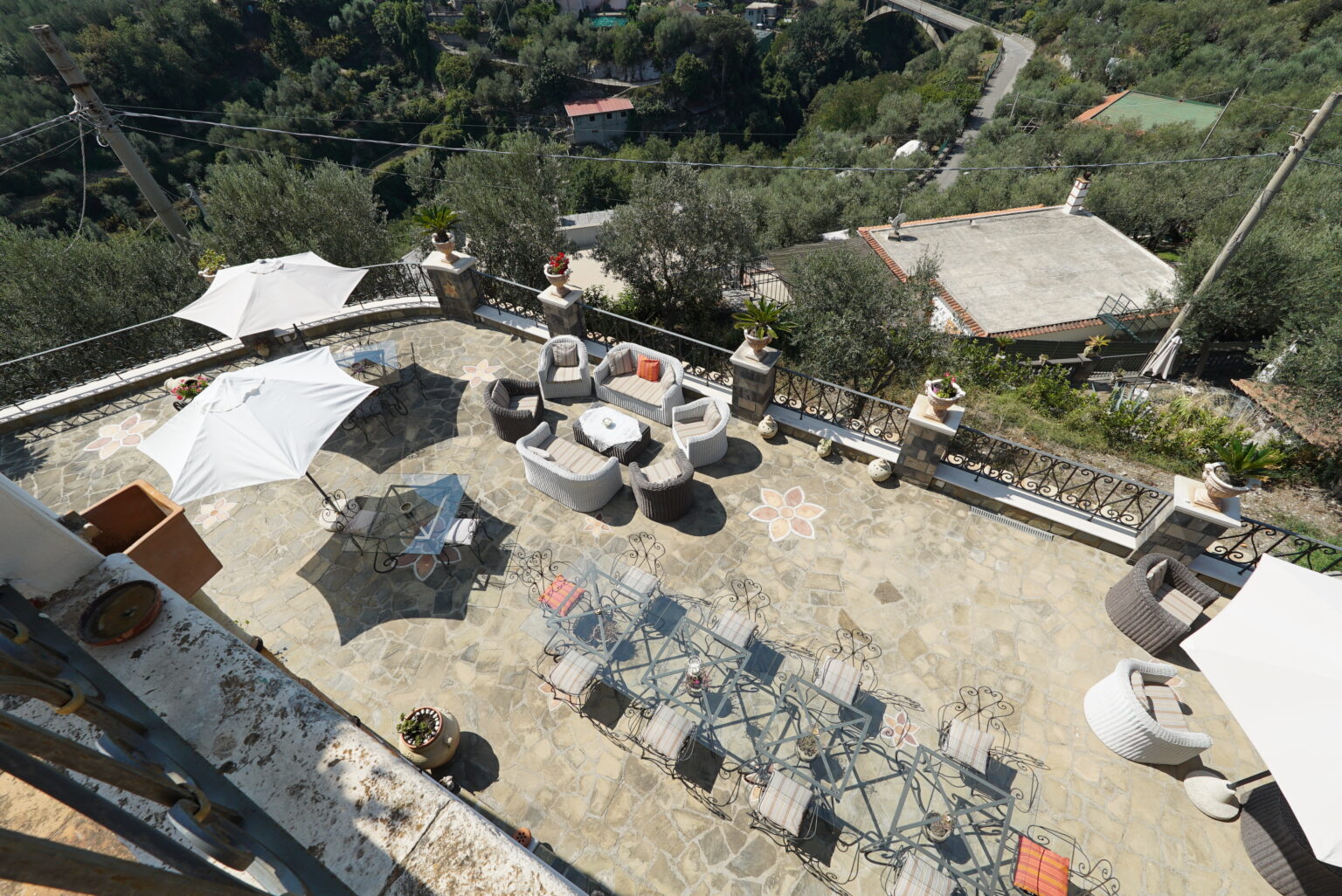 Aerial view of a spacious outdoor terrace with lounge furniture, umbrellas, and a scenic backdrop of greenery, ideal for relaxation and gatherings. | Only on SopranoVillas