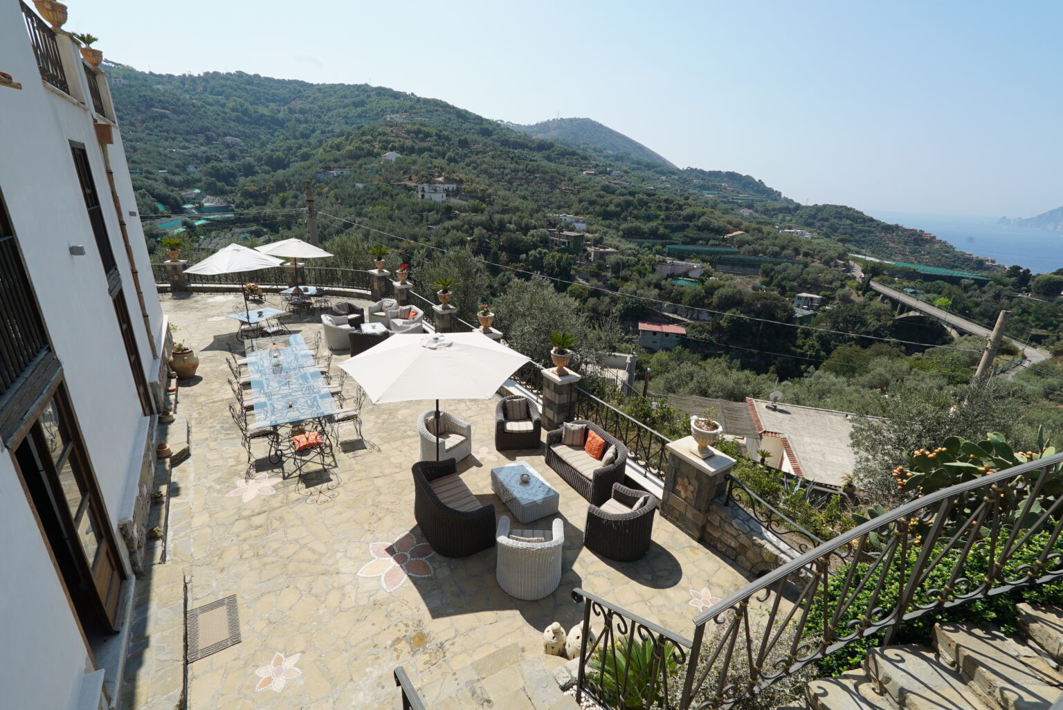 Scenic outdoor terrace with modern seating and dining area overlooking lush hills and coastline, ideal for relaxation and entertaining. | Only on SopranoVillas