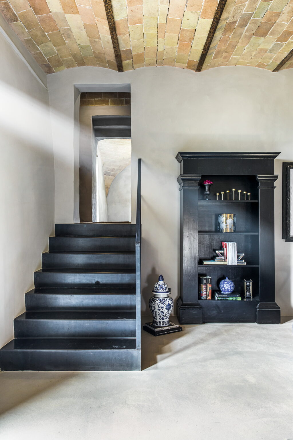 Black staircase leading to an upper level, with a stylish black bookshelf displaying decorative items and books, set against a light-colored wall. | Only on SopranoVillas