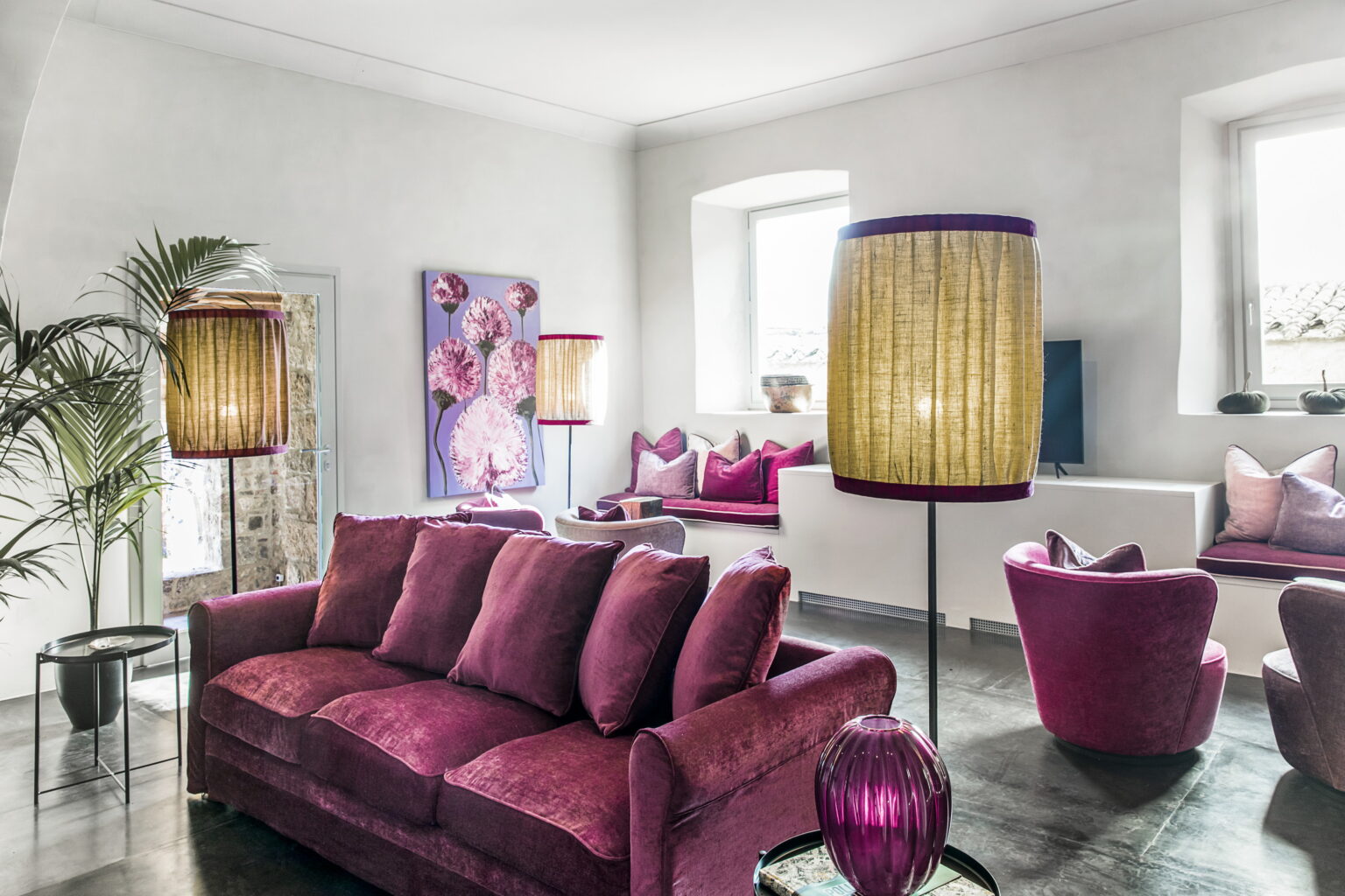Stylish modern living room featuring a plush purple sofa, vibrant floor lamps, and decorative cushions, complemented by floral artwork and a sleek design. | Only on SopranoVillas