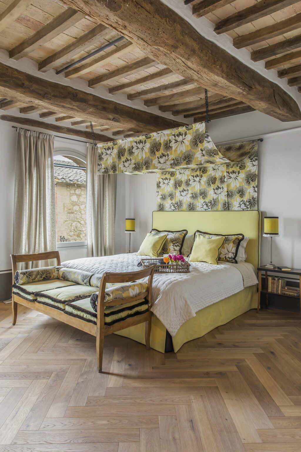 Cozy bedroom featuring a yellow and floral patterned headboard, coordinating pillows, and a decorative throw. Natural light streams through large windows, highlighting the elegant curtains and wooden furniture, creating a serene and inviting atmosphere. | Only on SopranoVillas