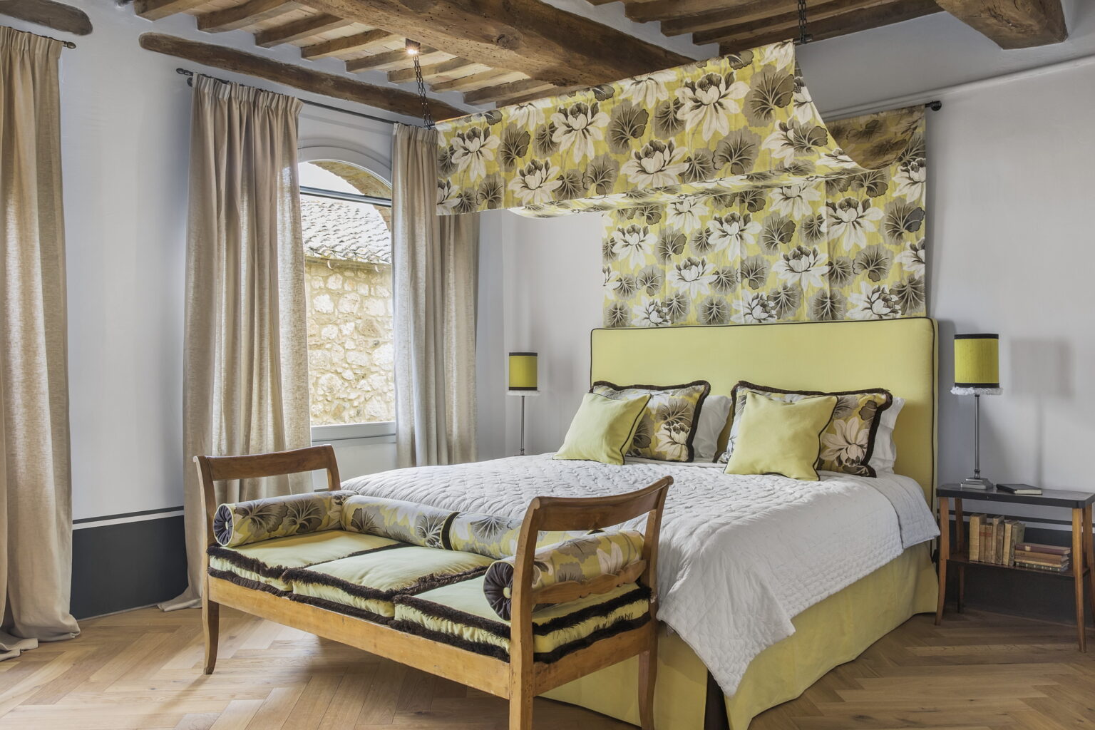 Stylish bedroom featuring a yellow and floral patterned headboard, cozy bedding, wooden beams, and large windows with draped curtains, creating a warm and inviting atmosphere. | Only on SopranoVillas