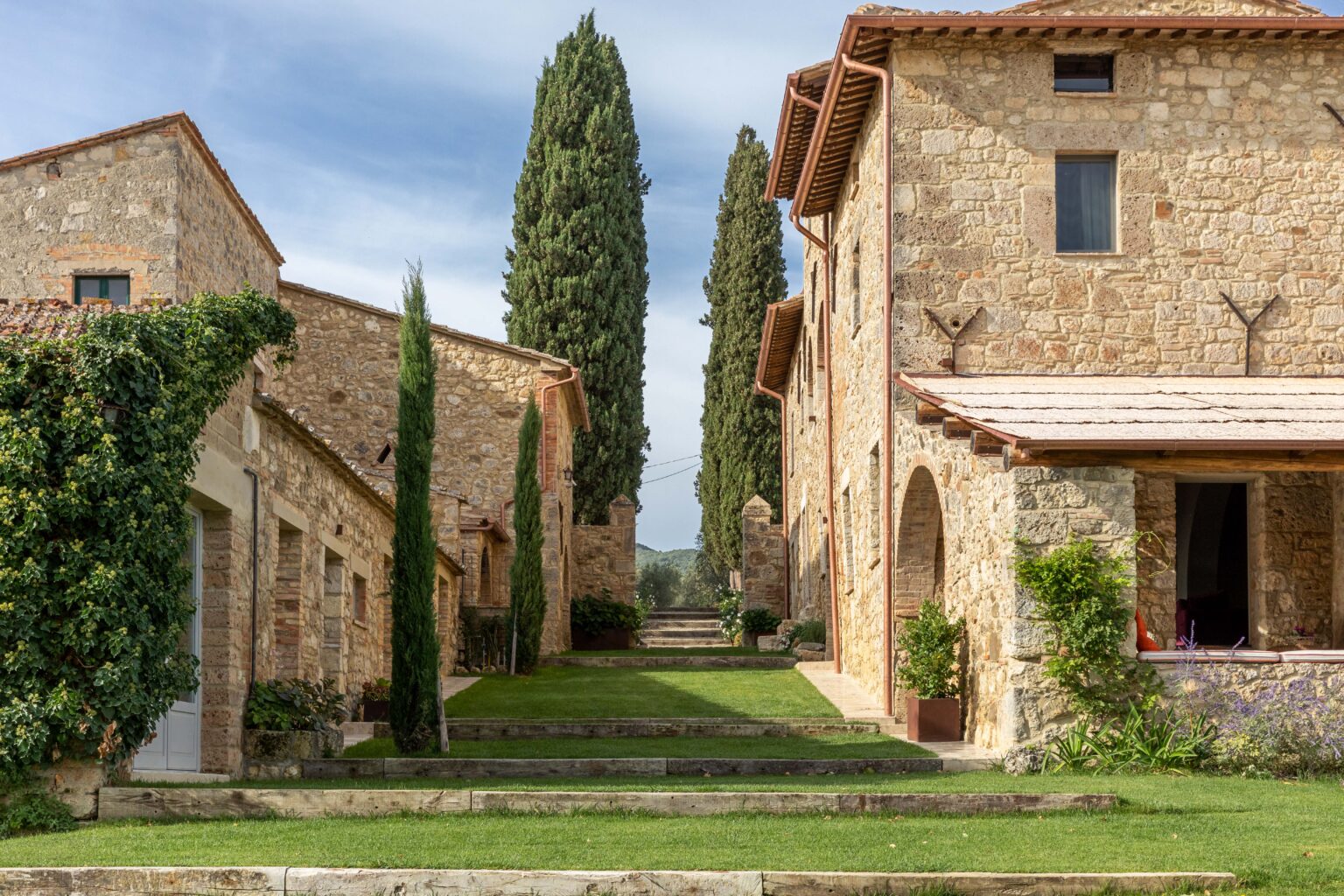 Stone buildings with rustic architecture surrounded by lush greenery and cypress trees in a serene landscape. Ideal for showcasing Tuscan countryside charm and outdoor living spaces. | Only on SopranoVillas