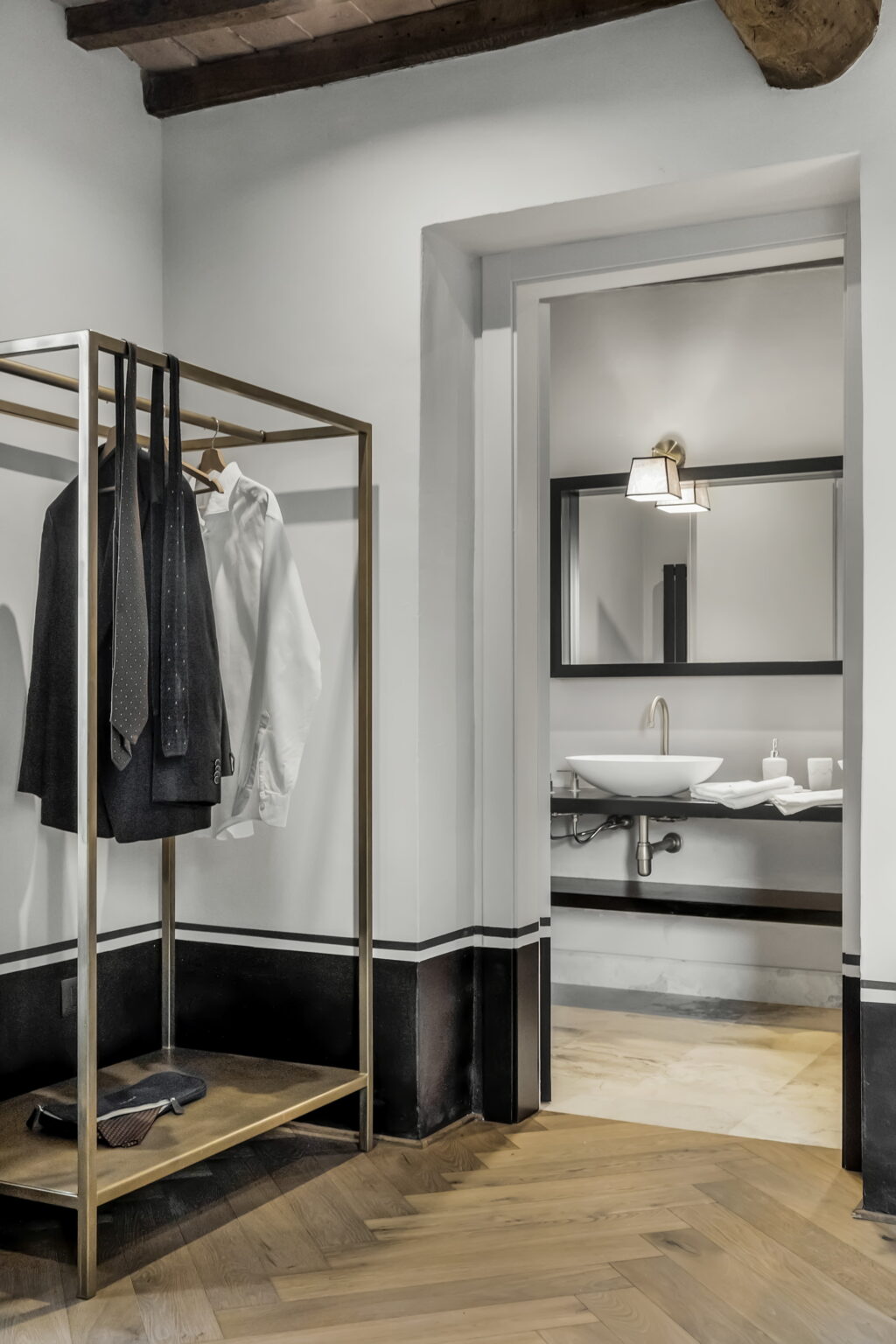 Stylish hotel room featuring a clothing rack with neatly hung shirts and ties, a modern bathroom with a sleek sink and mirror, and contemporary lighting. | Only on SopranoVillas