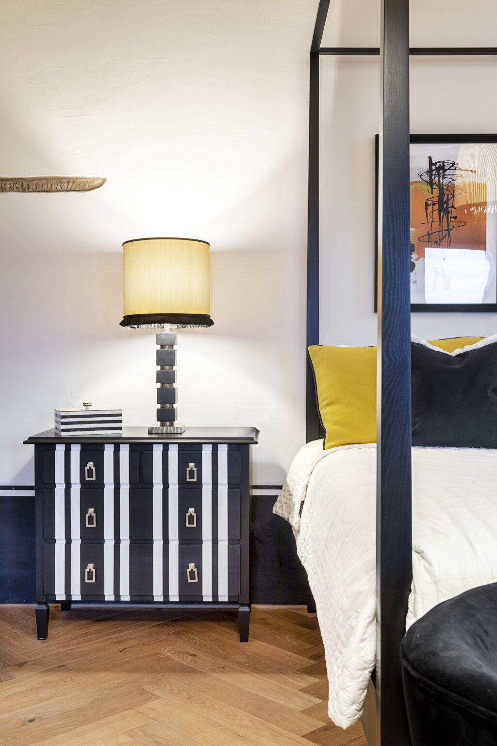 Modern bedroom interior featuring a stylish black and white nightstand, a decorative lamp with a beige shade, and vibrant yellow and black cushions on the bed. The design combines contemporary aesthetics with a touch of elegance. | Only on SopranoVillas