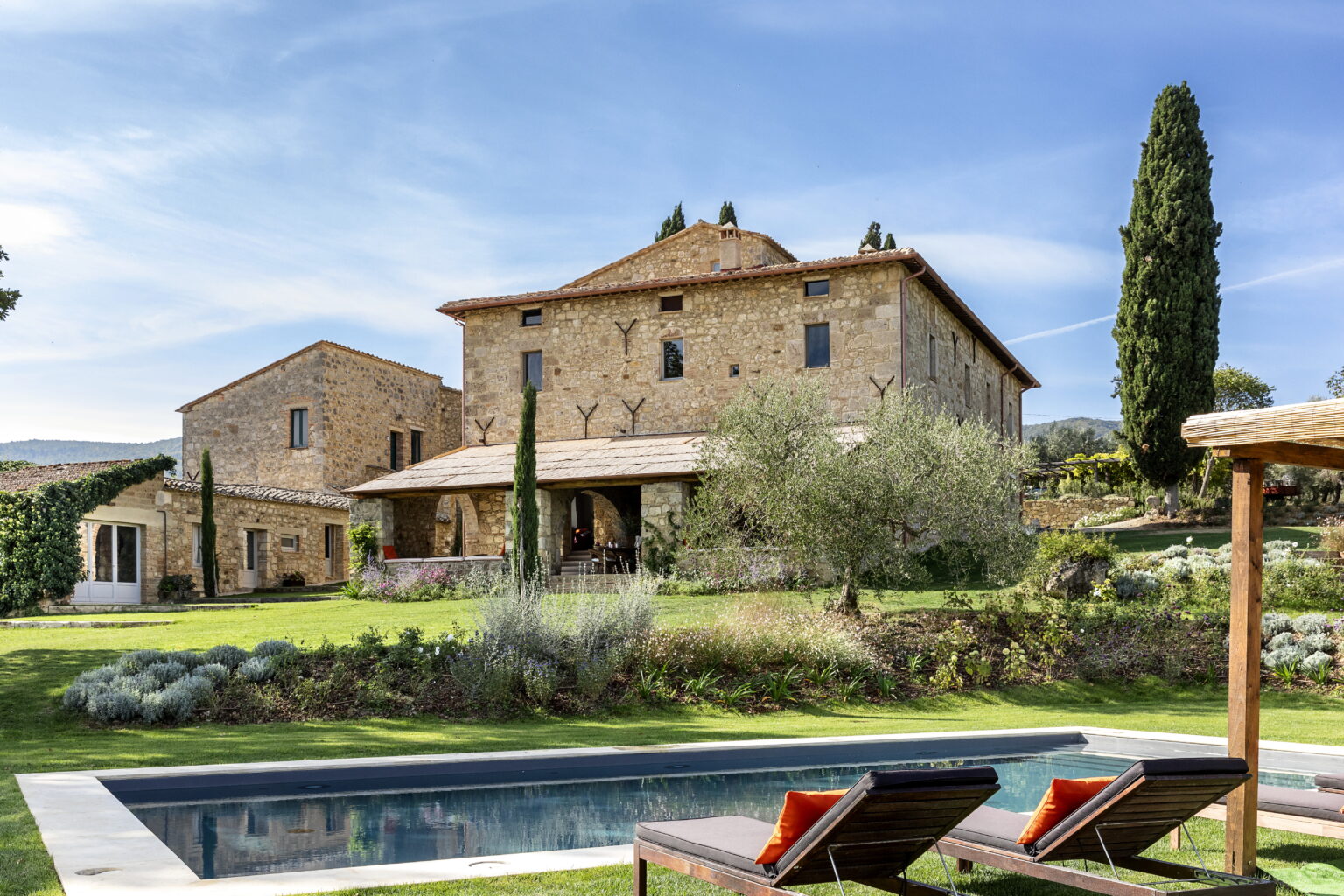 Rustic stone villa with a swimming pool, surrounded by lush greenery and cypress trees, set against a clear blue sky. Ideal for luxury getaways and outdoor relaxation. | Only on SopranoVillas