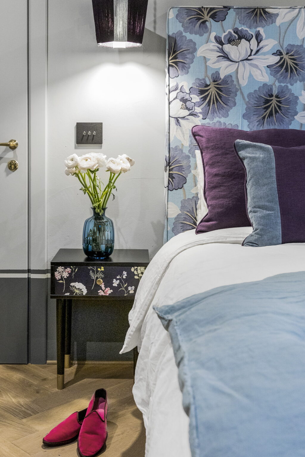 Cozy bedroom corner featuring a neatly made bed with decorative pillows, a stylish bedside table with floral design, and a vibrant vase of fresh flowers, creating an inviting and elegant atmosphere. | Only on SopranoVillas