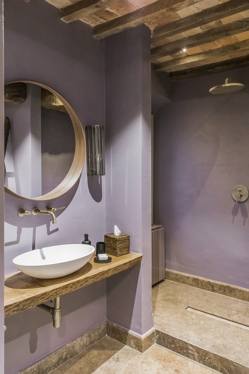 Modern bathroom featuring a circular mirror, a sleek white sink, and a stylish wooden countertop. The walls are painted in a soothing lavender color, creating a calming atmosphere. The space includes elegant fixtures and minimalist decor for a contemporary look. | Only on SopranoVillas