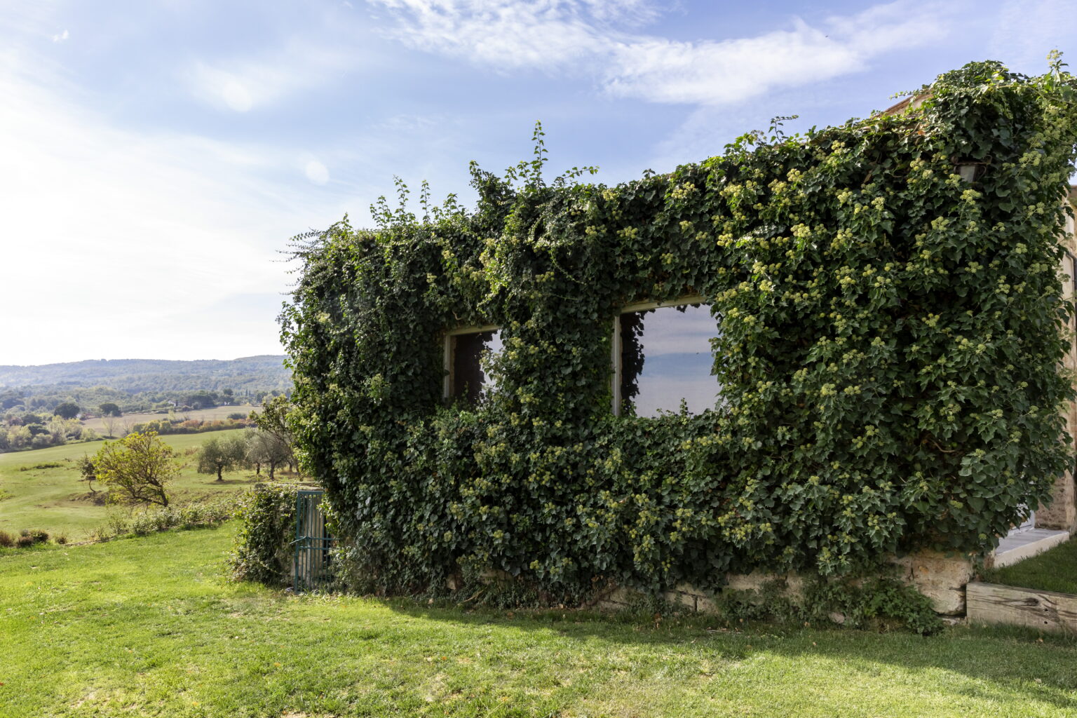 Abandoned building covered in lush green ivy, set against a scenic landscape with rolling hills and blue skies. | Only on SopranoVillas