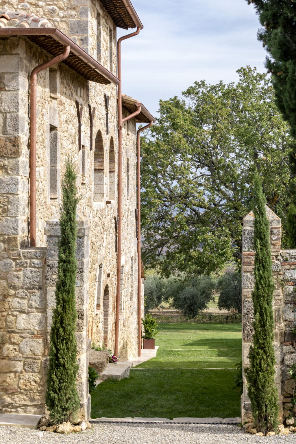 Historic stone building with arched windows, framed by tall cypress trees, set against a backdrop of lush greenery in a serene landscape. Ideal for showcasing architectural beauty and natural surroundings. | Only on SopranoVillas