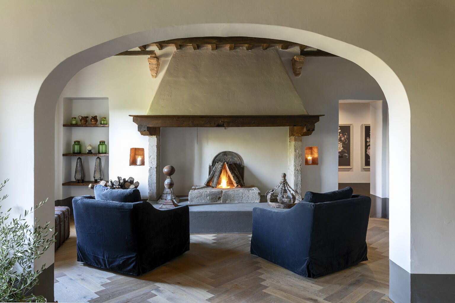 Cozy living room featuring a modern fireplace, two dark blue armchairs, and warm lighting, framed by an elegant archway and wooden beams overhead. | Only on SopranoVillas