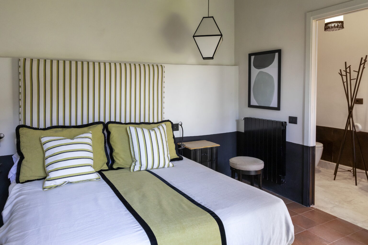 Modern bedroom design featuring a striped headboard, decorative pillows in green and white, and minimalist decor. The room includes a small side table and a stylish lamp, creating a cozy and inviting atmosphere. | Only on SopranoVillas