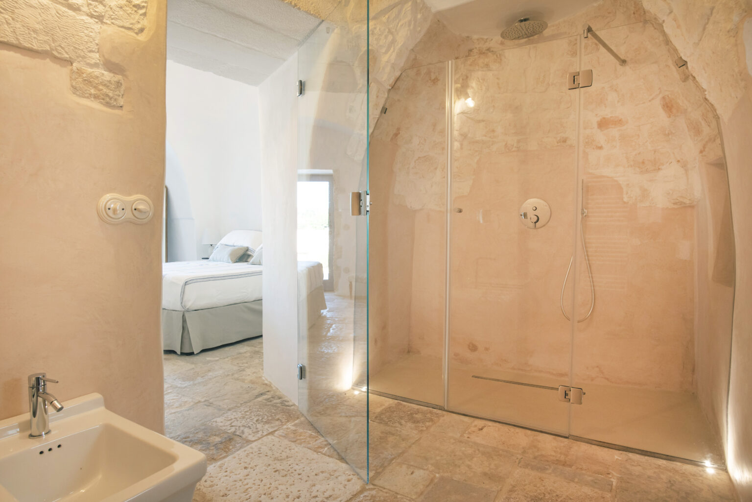 Modern bathroom featuring a spacious glass shower with natural stone walls, a sleek sink, and a soft color palette, creating a serene and elegant atmosphere. | Only on SopranoVillas