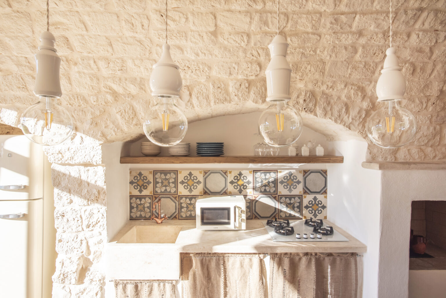 Modern kitchen interior featuring stone walls, decorative tiled backsplash, gas stove, and pendant lighting. The design combines rustic elements with contemporary style, creating a warm and inviting atmosphere. | Only on SopranoVillas