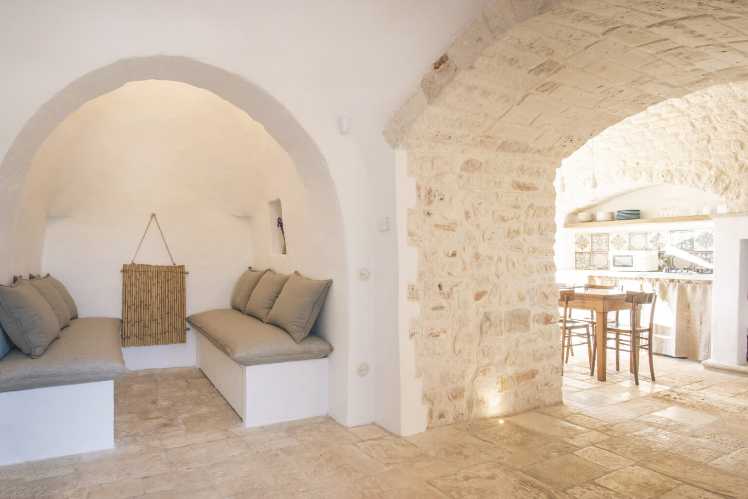 Cozy interior of a modern rustic home featuring arched stone walls, comfortable seating areas with gray cushions, and a bright open kitchen space in the background. | Only on SopranoVillas