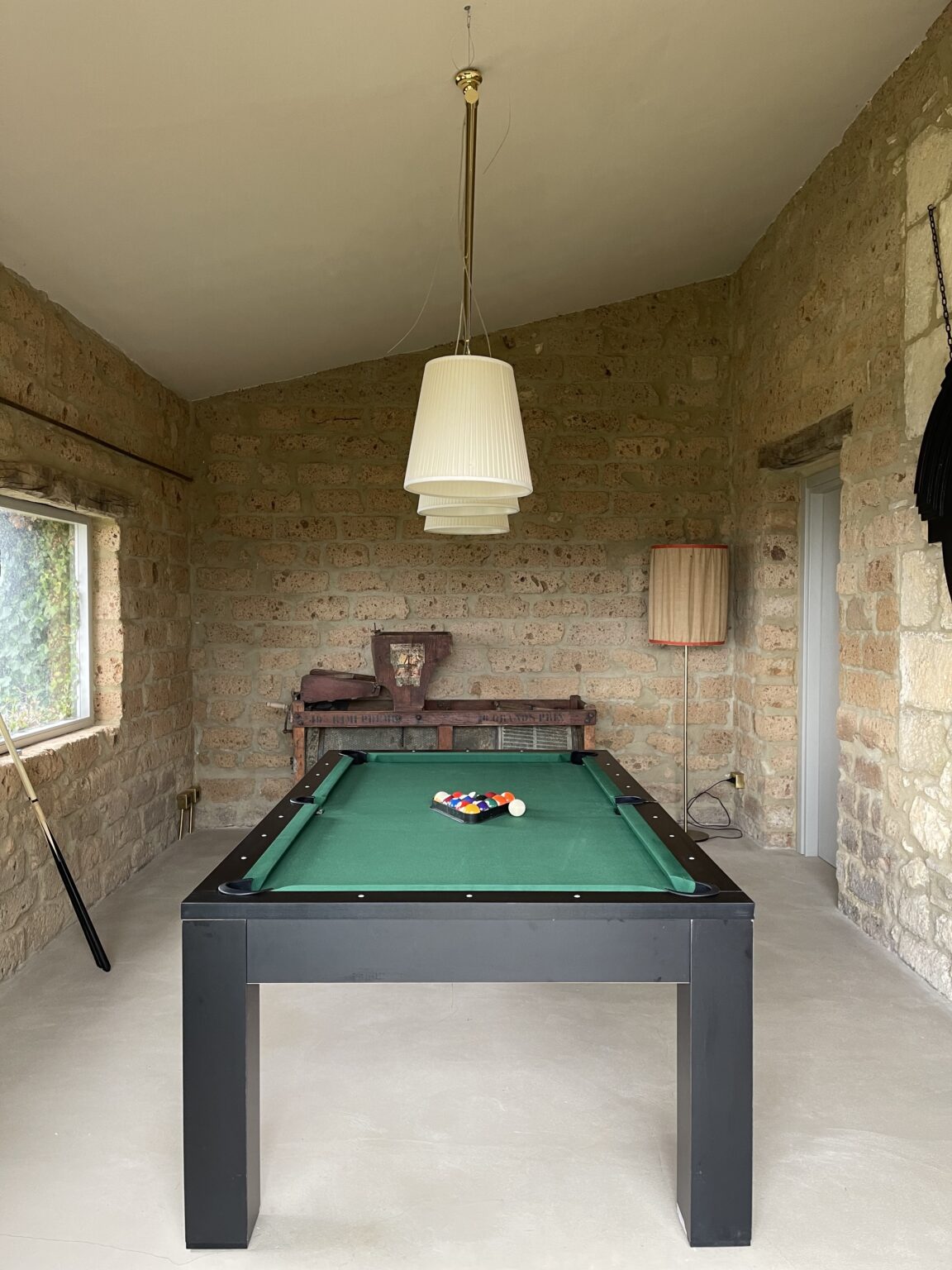 Interior view of a rustic game room featuring a green pool table with a set of billiard balls, stone walls, and pendant lighting. | Only on SopranoVillas