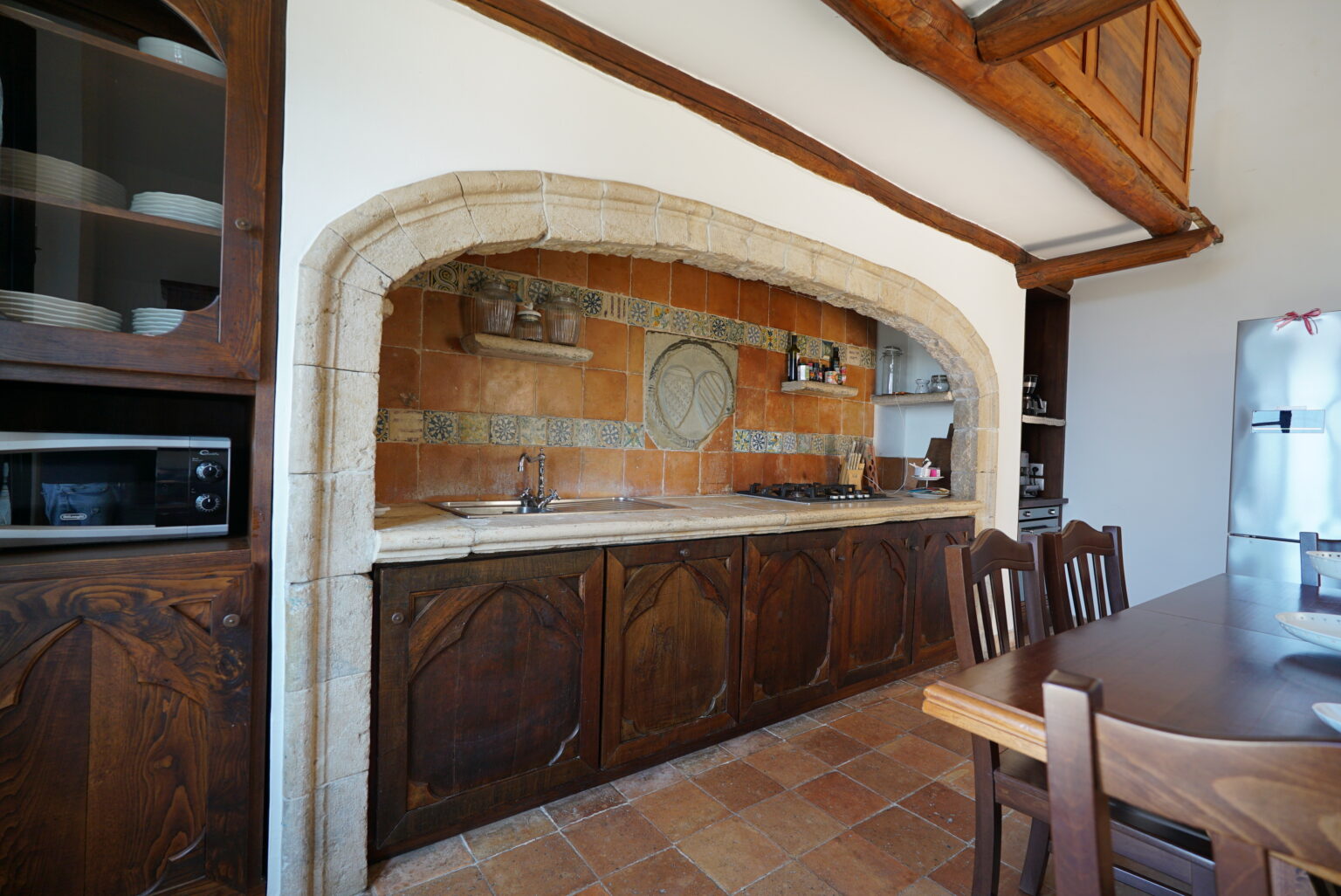 Rustic kitchen interior featuring a stone archway, wooden cabinetry, and a tiled backsplash, with a dining table and modern appliances visible. | Only on SopranoVillas