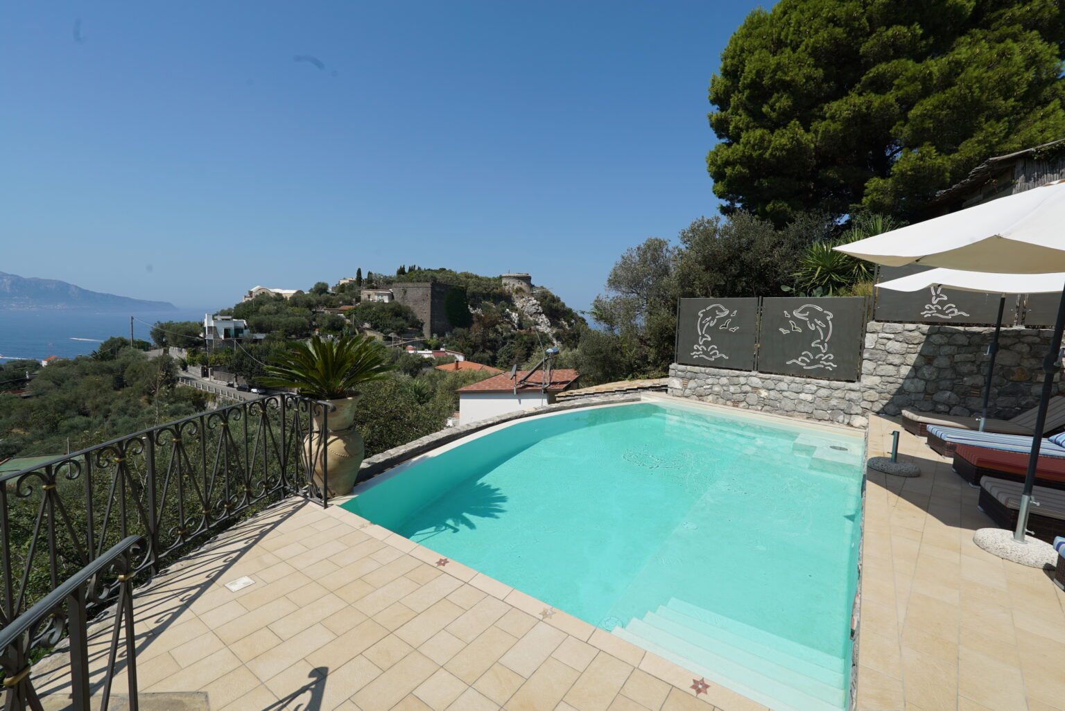 Luxury villa with a private swimming pool overlooking a scenic landscape, featuring a tiled patio and lush greenery under a clear blue sky. | Only on SopranoVillas