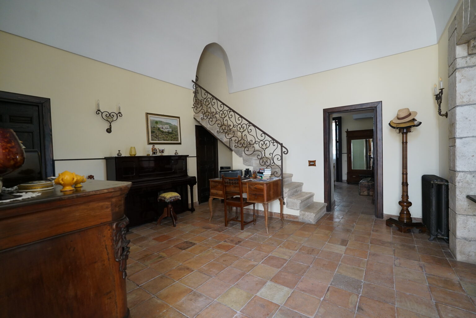 Spacious interior of a classic home featuring a staircase, wooden furniture, and decorative elements, with terracotta tile flooring and natural light illuminating the room. | Only on SopranoVillas