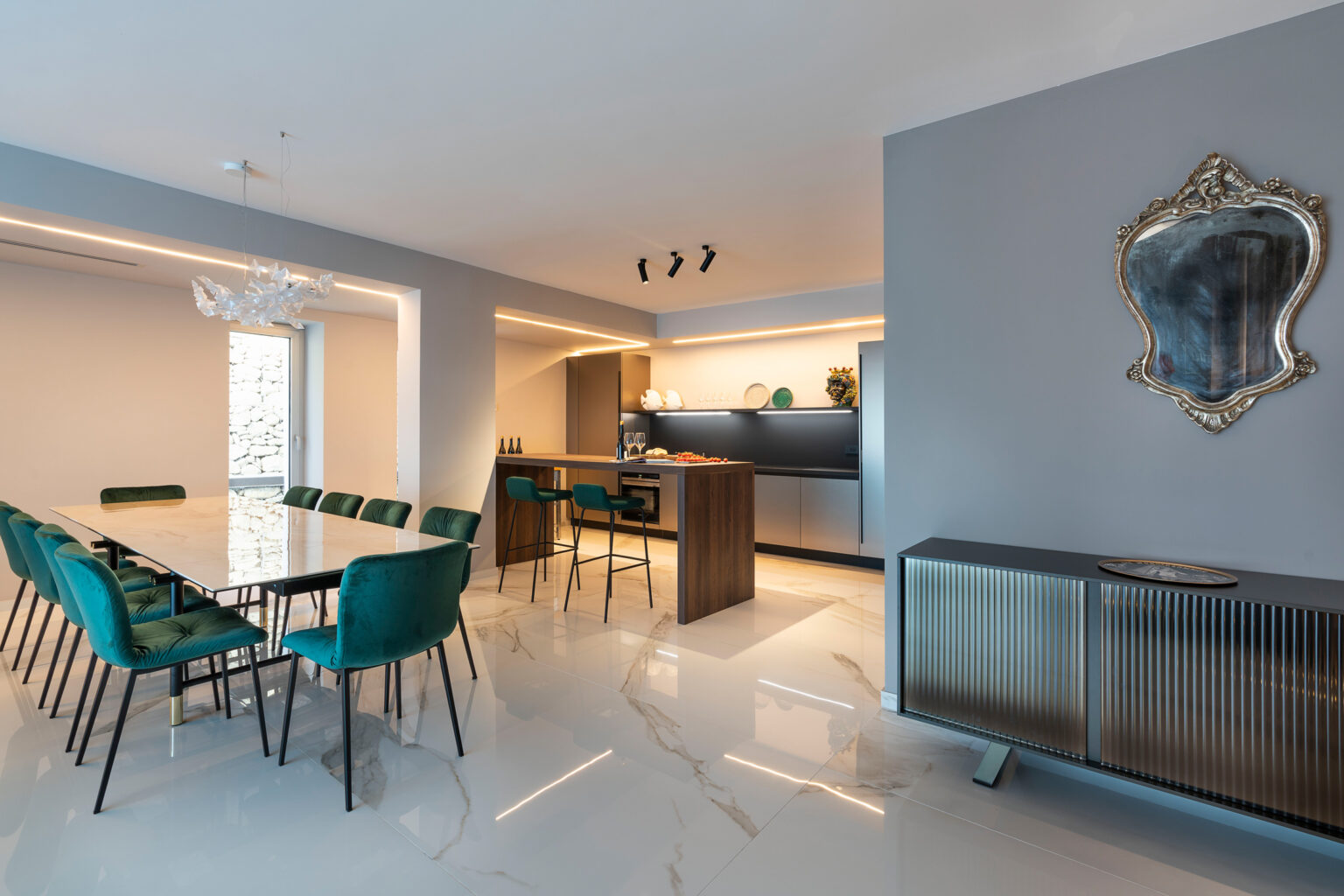 Modern dining area featuring a sleek table with green chairs, an open kitchen with contemporary appliances, and stylish decor including a decorative mirror and elegant lighting. | Only on SopranoVillas