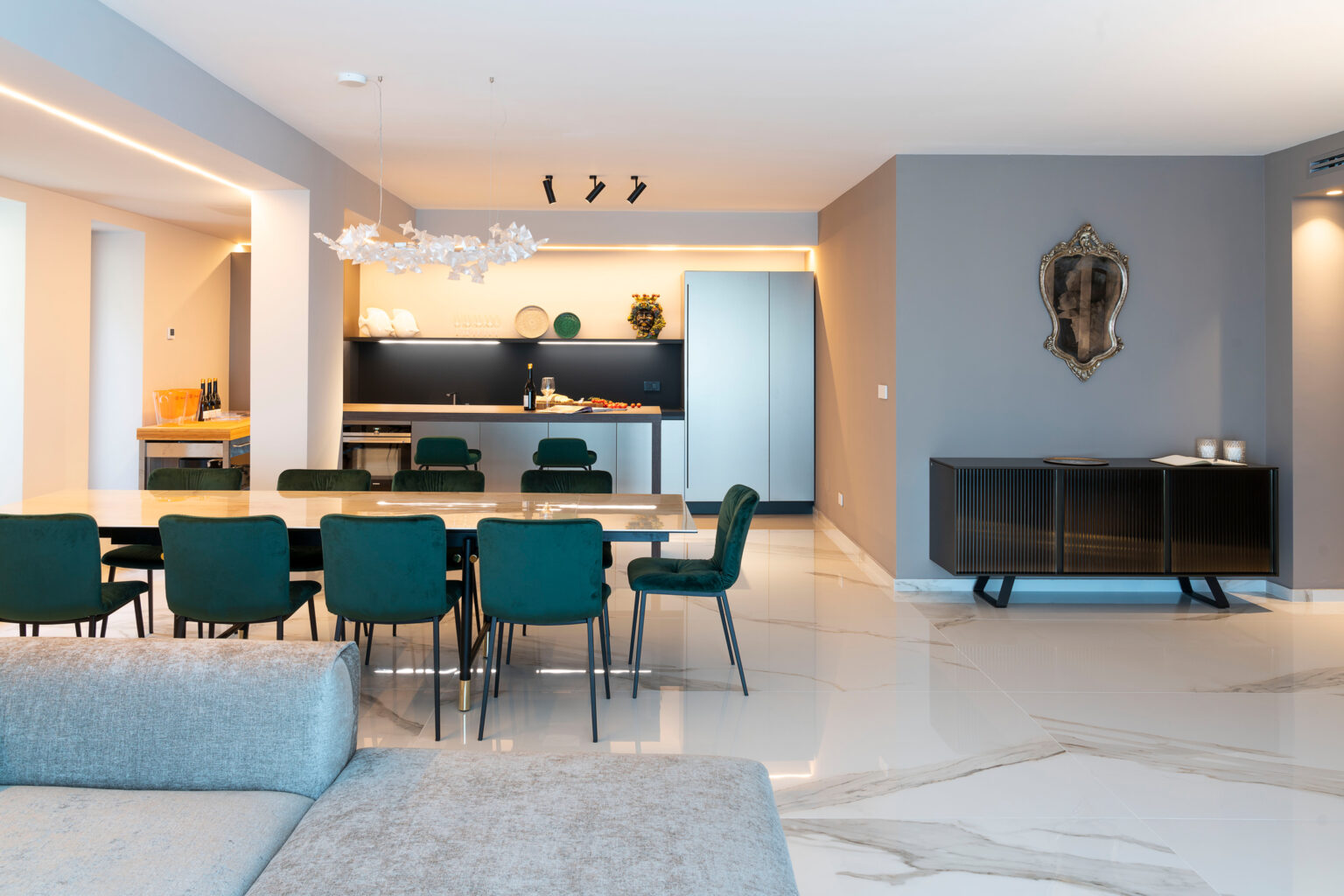 Modern open-concept living space featuring a dining area with green chairs, a sleek kitchen with contemporary appliances, and stylish decor elements. The room is illuminated by natural light and has a neutral color palette. | Only on SopranoVillas