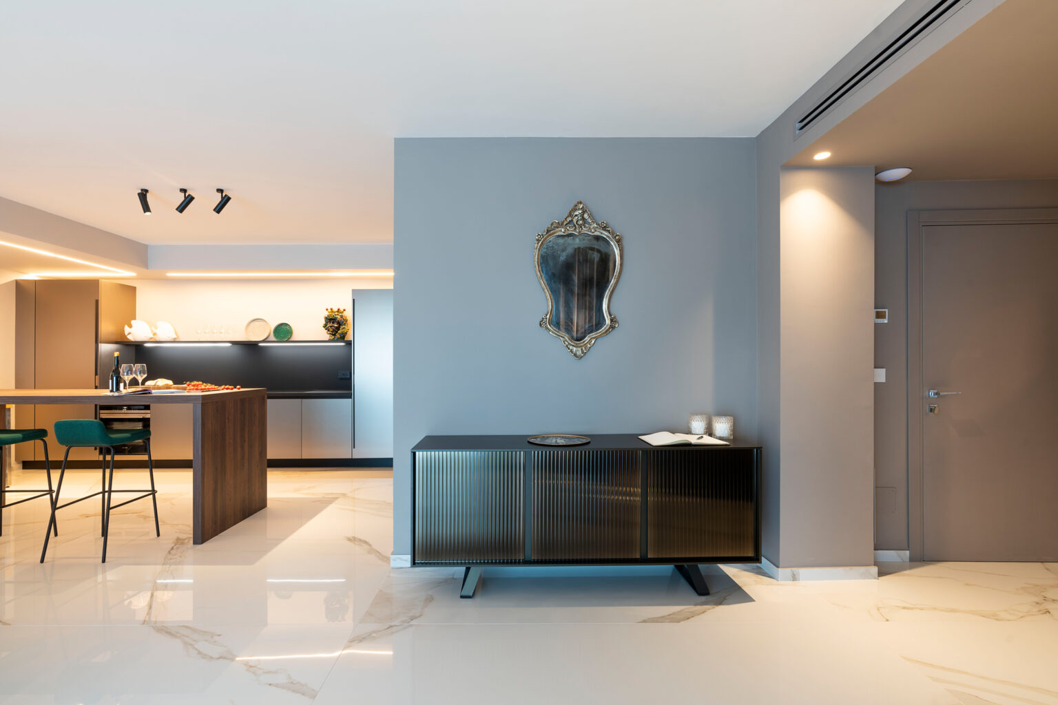 Modern living room interior featuring a sleek sideboard, stylish mirror, and contemporary kitchen in the background. The space is illuminated with soft lighting and showcases elegant marble flooring. | Only on SopranoVillas