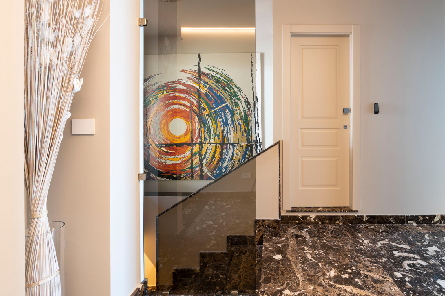 Modern interior hallway featuring a colorful abstract painting, sleek glass railing, and polished marble flooring, with decorative dried flowers in a vase. | Only on SopranoVillas