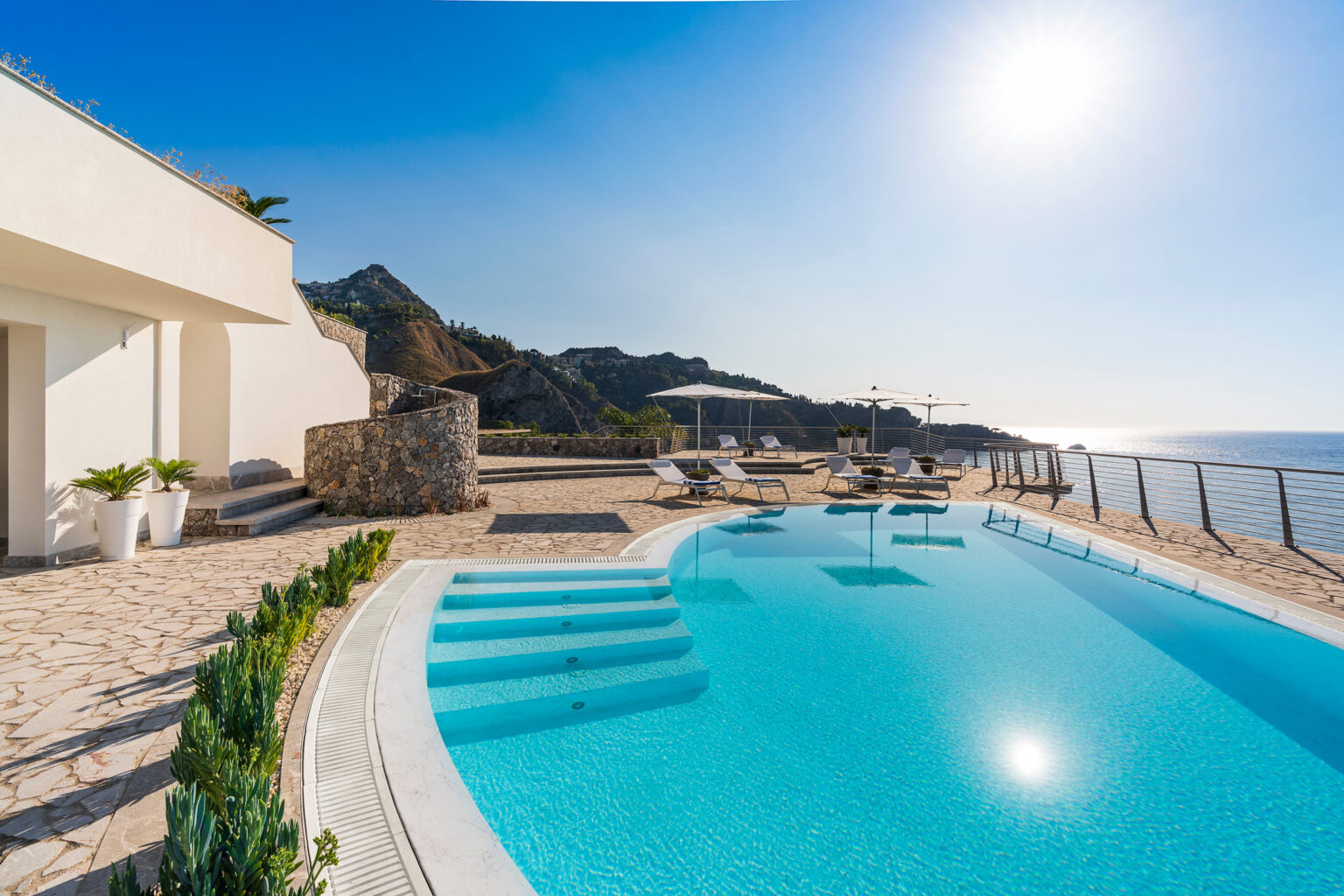 Luxury villa with a stunning ocean view, featuring a sparkling infinity pool, sun loungers, and a spacious terrace under a clear blue sky. Ideal for relaxation and outdoor gatherings. | Only on SopranoVillas
