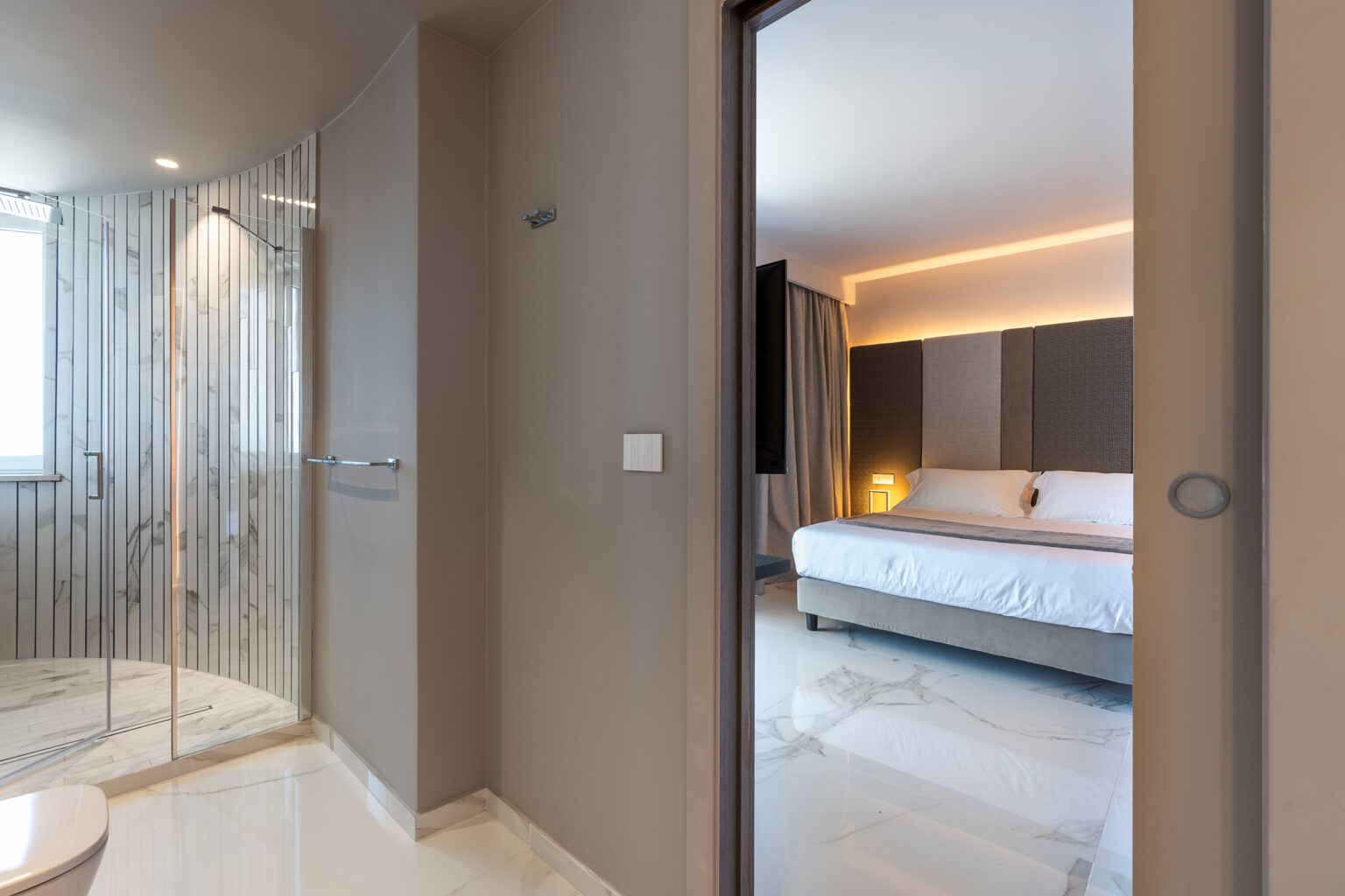 Modern hotel room interior featuring a stylish bedroom with ambient lighting and a glass-enclosed shower area, showcasing contemporary design and luxury amenities. | Only on SopranoVillas