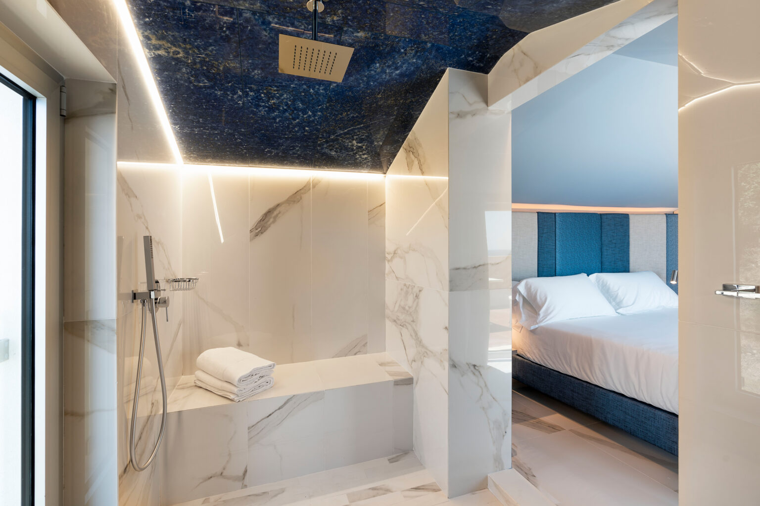 Luxurious bathroom featuring a spacious shower with marble walls, modern fixtures, and a stylish blue ceiling, leading to a cozy bedroom with a comfortable bed. | Only on SopranoVillas