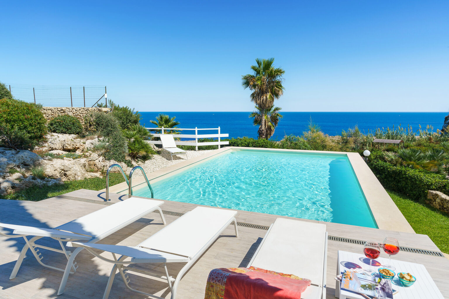 Luxury villa with a swimming pool overlooking the ocean, surrounded by lush greenery and sun loungers, ideal for a relaxing getaway. | Only on SopranoVillas