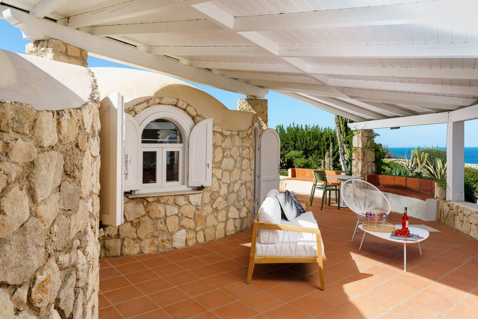 Spacious outdoor patio with stone walls, modern seating, and ocean views, featuring a shaded area under a white pergola. | Only on SopranoVillas