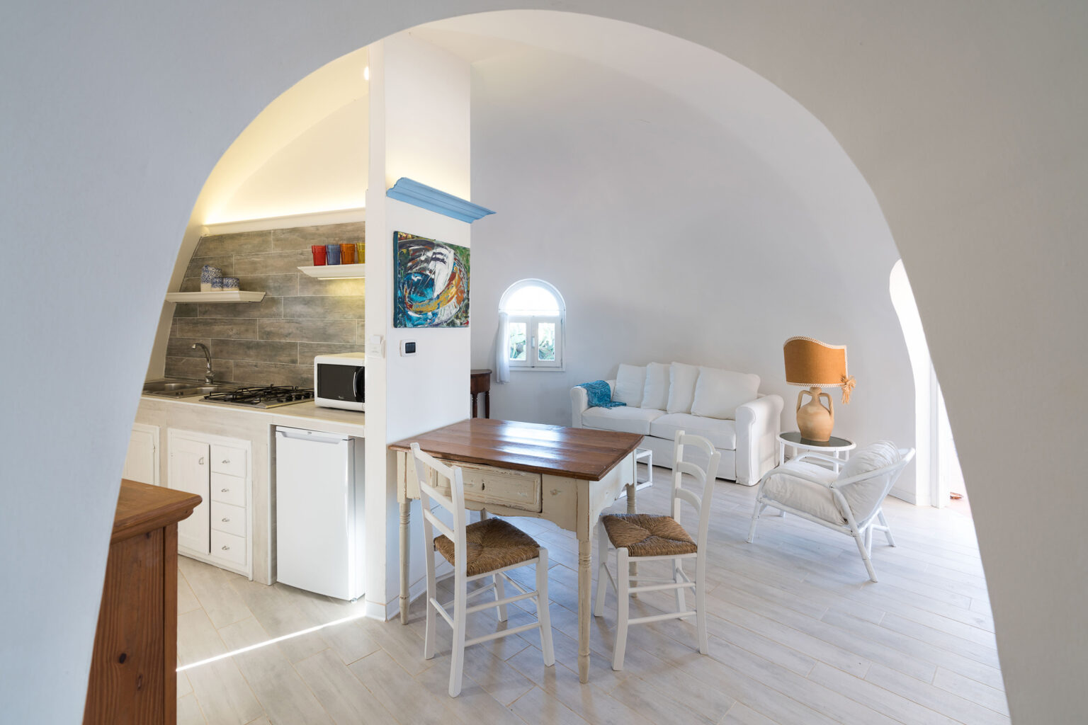 Cozy and modern interior of a bright, minimalist kitchen and living area featuring white walls, wooden furniture, and an archway design, ideal for small space living. | Only on SopranoVillas