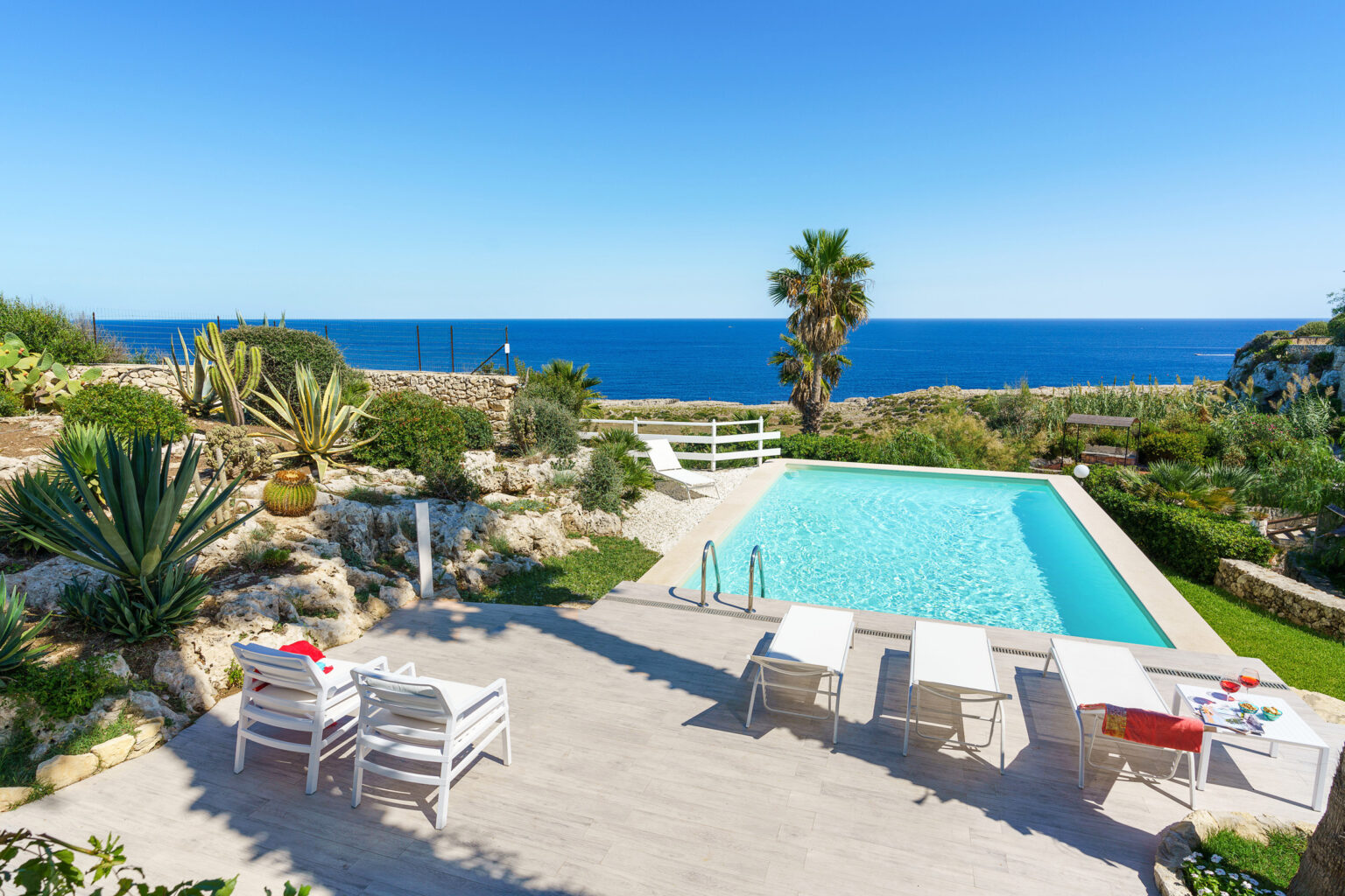 Luxury seaside villa with a swimming pool, surrounded by tropical plants and a clear blue ocean in the background, perfect for relaxation and vacation getaways. | Only on SopranoVillas