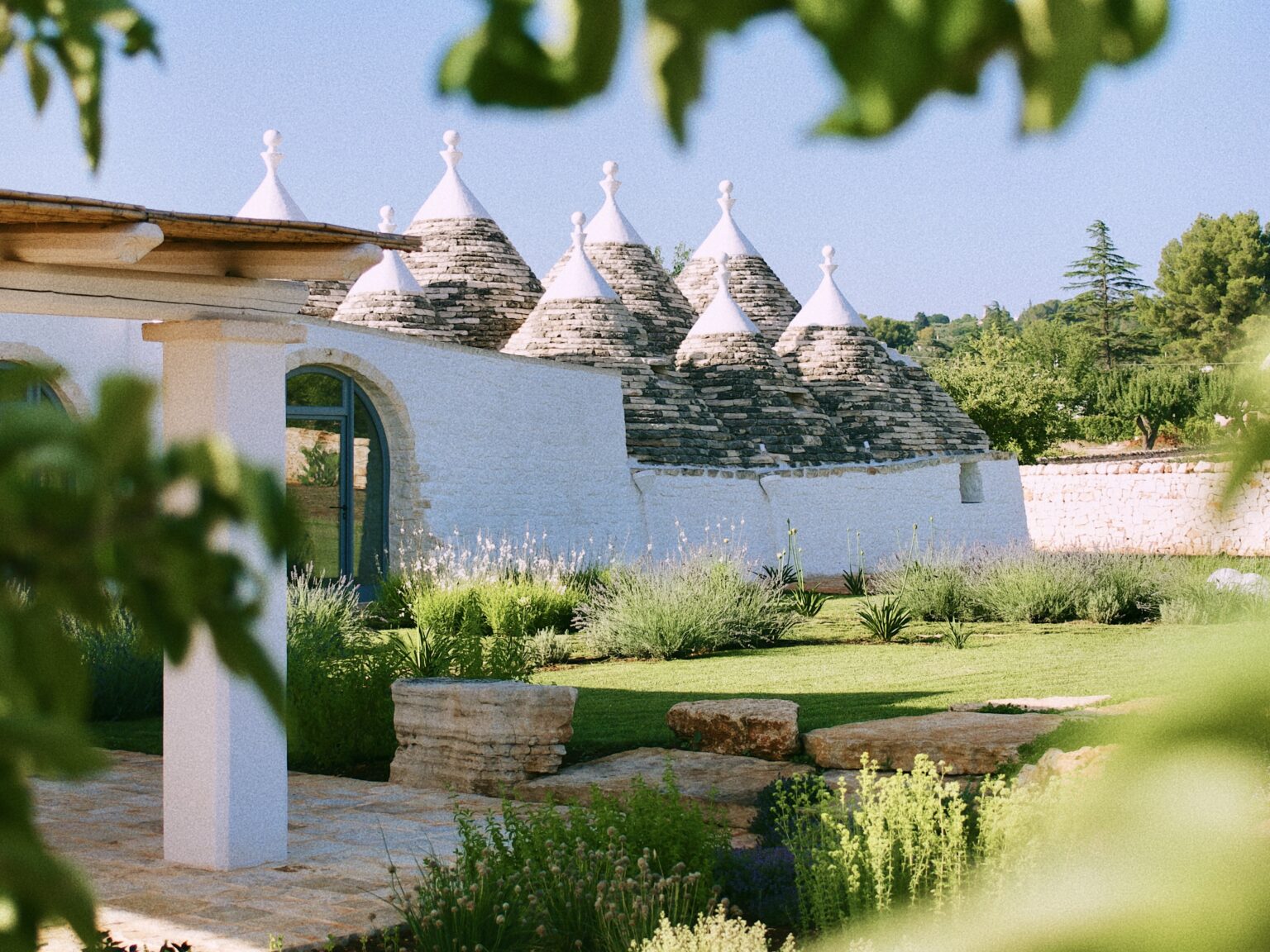 Trulli houses with conical roofs surrounded by lush greenery in a serene garden setting. | Only on SopranoVillas